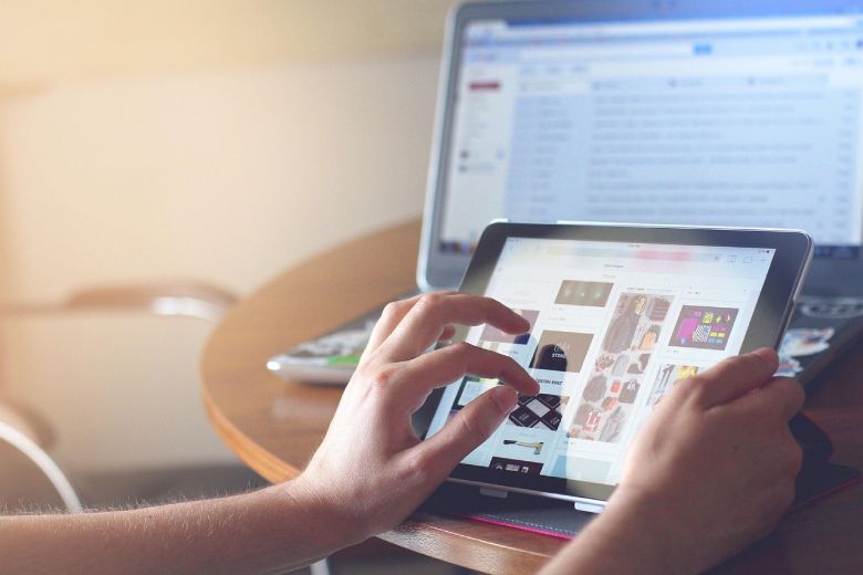 Person using a tablet computer, with a laptop in the background, likely browsing a website with Digital Ads
