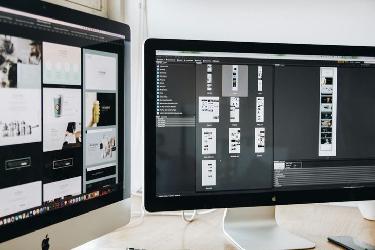 Two computer monitors displaying design work, likely for a website or app, on a desk.