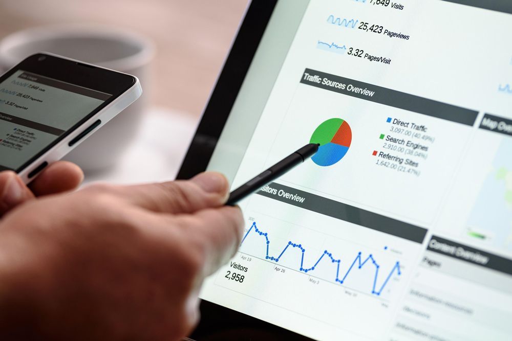 Person pointing at a pie chart on a tablet screen, holding a phone. Business analysis.