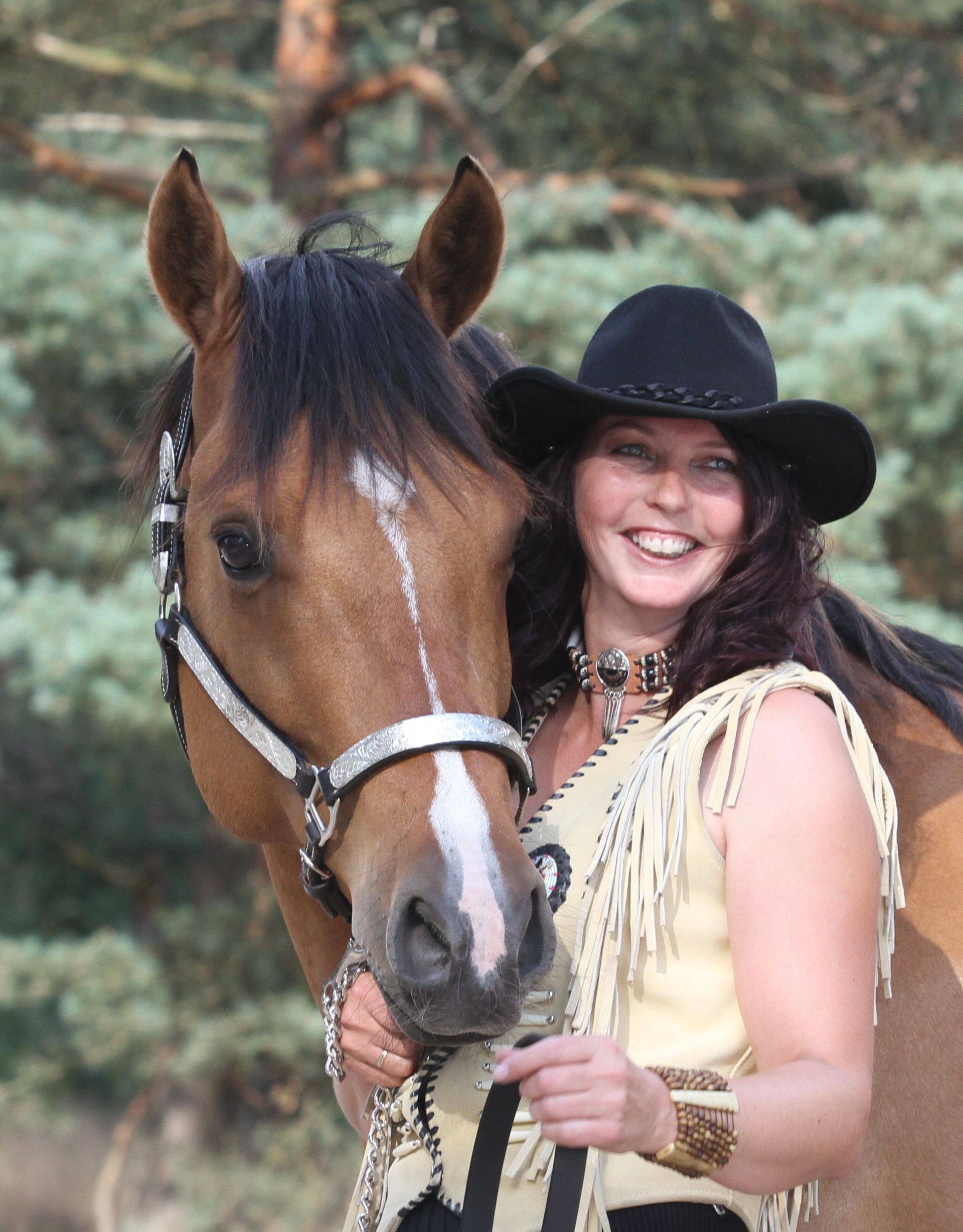 Een vrouw met een cowboyhoed staat naast een bruin paard