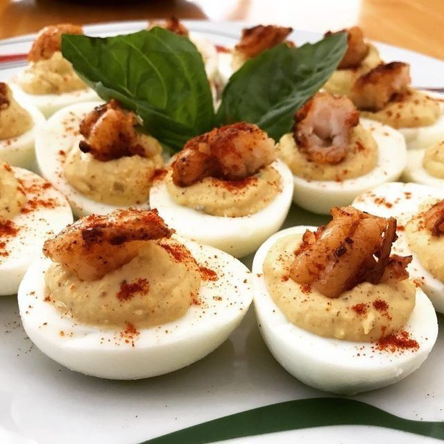 Deviled eggs on a plate, topped with meat and paprika, garnished with basil leaves.