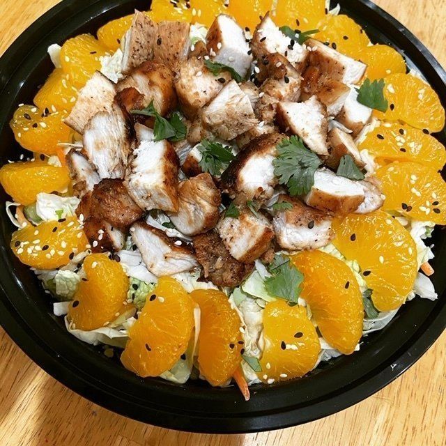Chicken salad with mandarin oranges, sesame seeds, and cilantro in a black bowl.