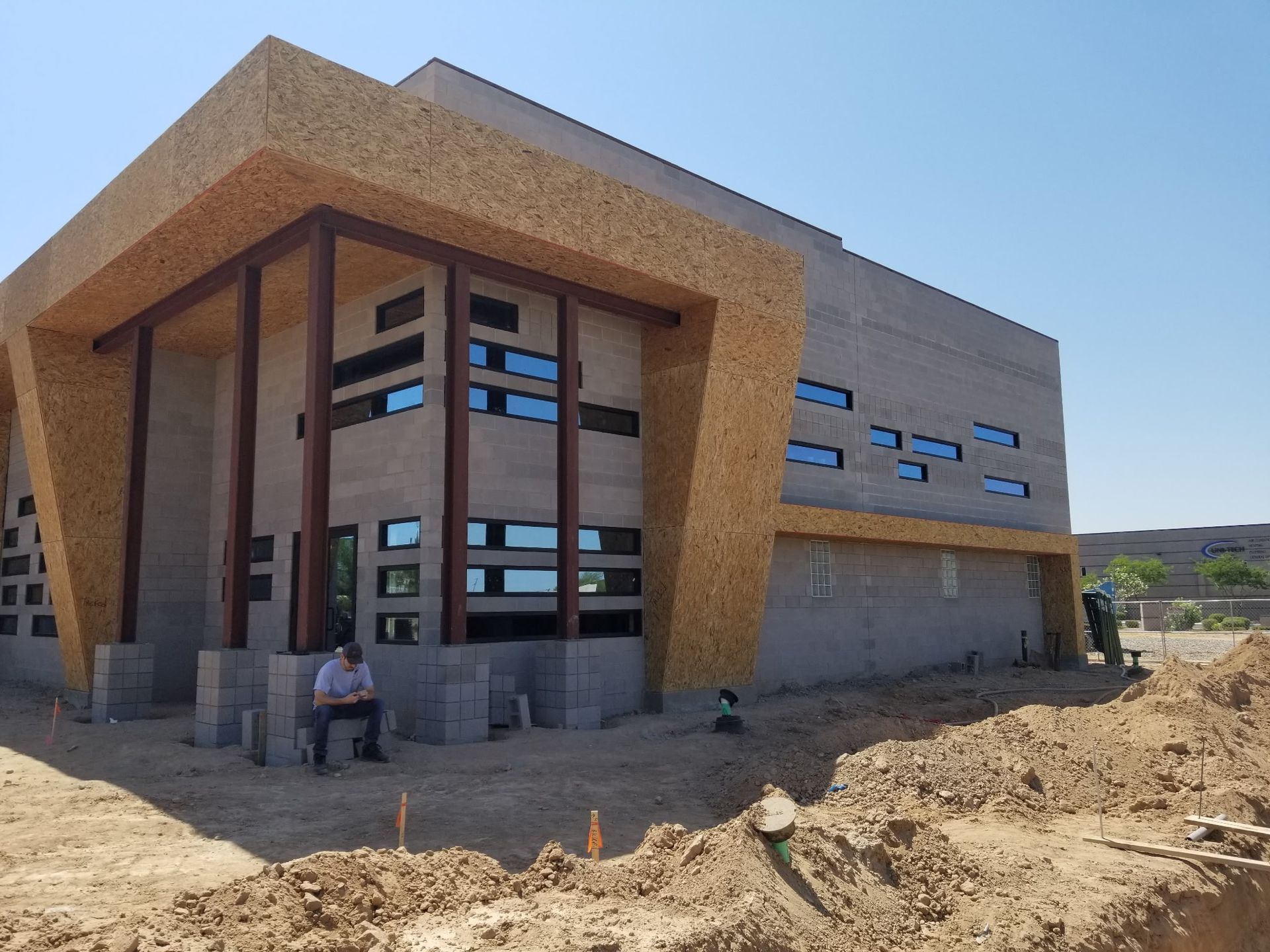 Modern unfinished tan building with large windows and a person sitting by the entrance