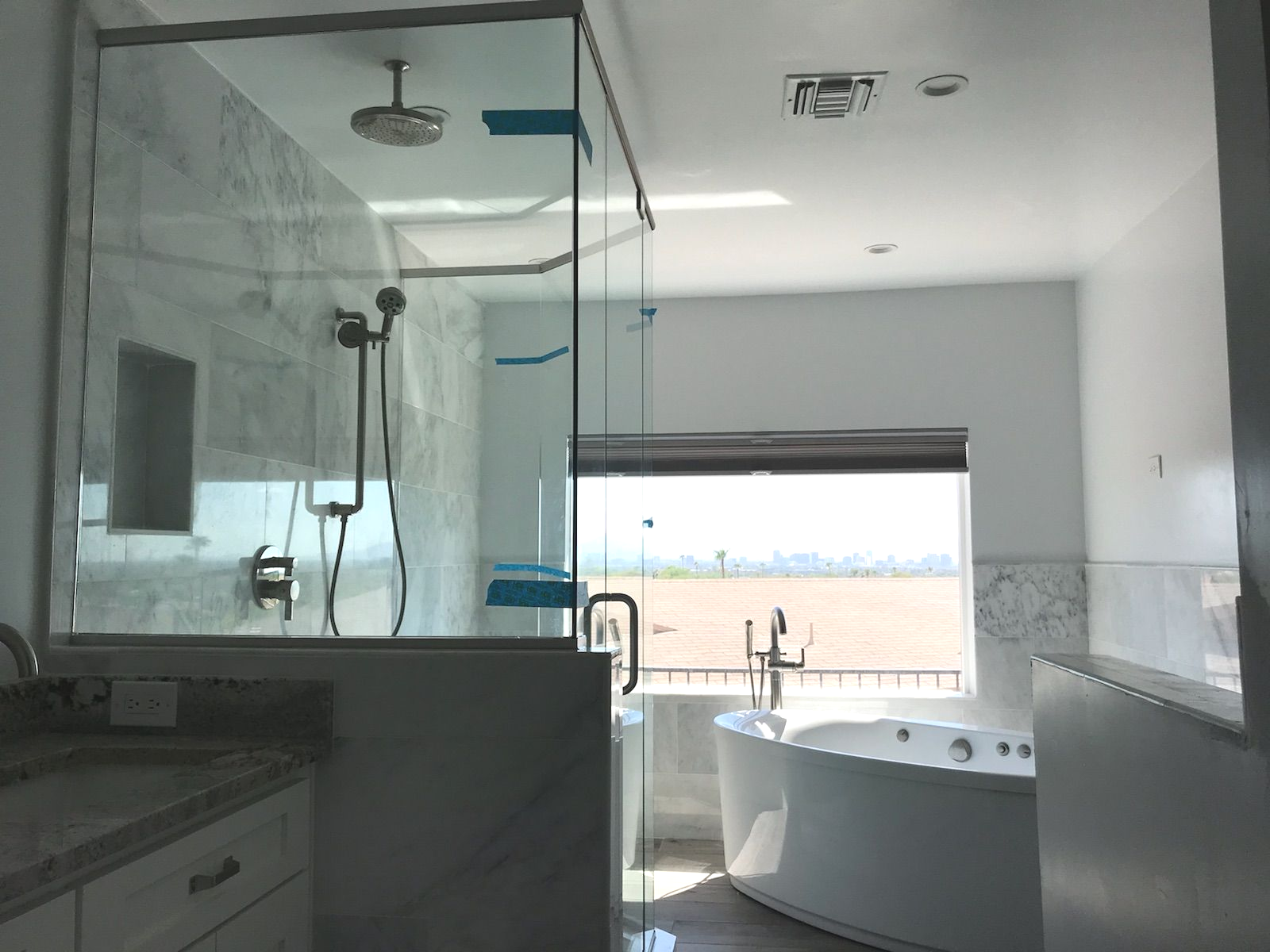 Spacious bathroom with a glass shower, bathtub, and a window overlooking a cityscape.