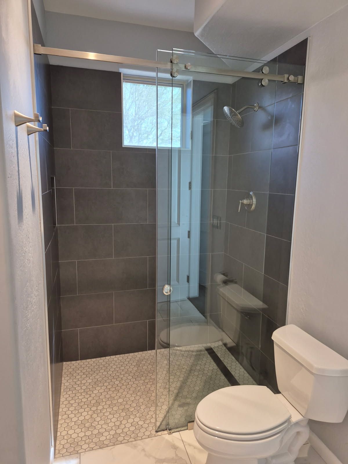 Modern bathroom with a glass shower, dark gray tile walls, and a toilet.