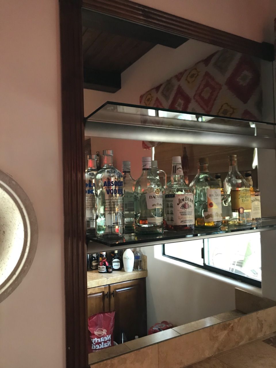 Mirror reflects a home bar with liquor bottles, a sink, and a cabinet.
