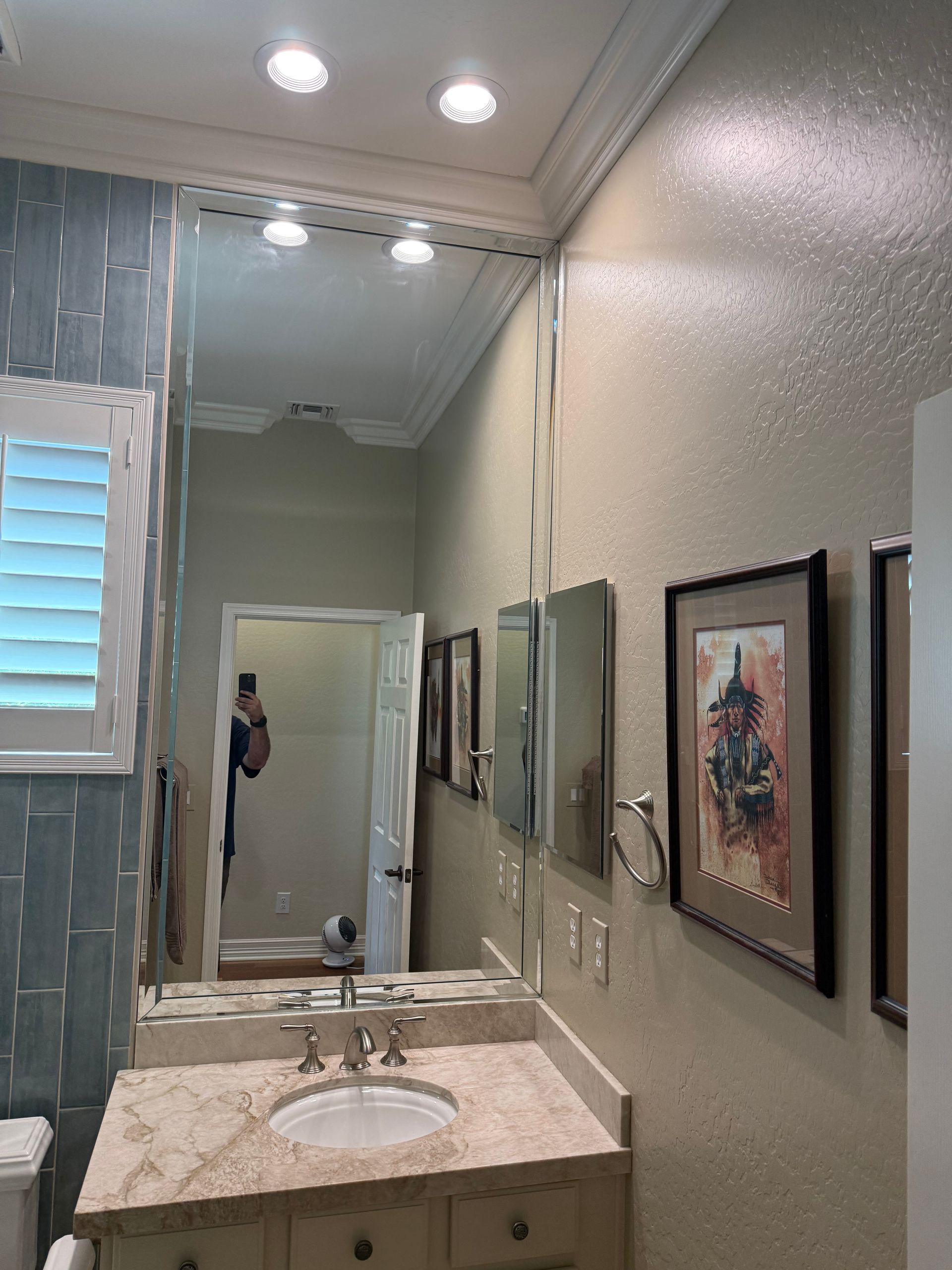 Bathroom with large mirror above vanity, blue tile wall, artwork.