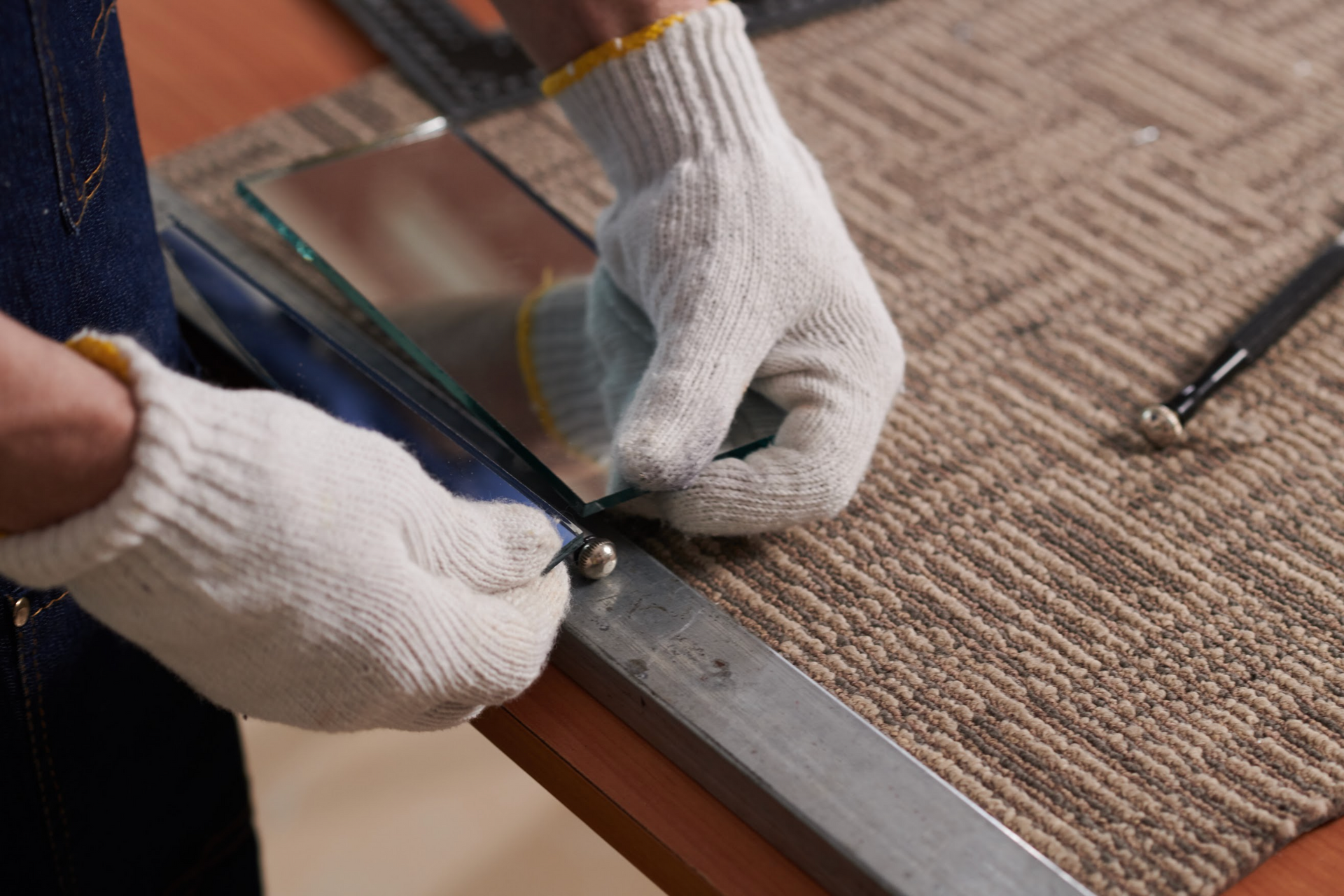 Person wearing gloves cutting glass with a tool, on a patterned surface.