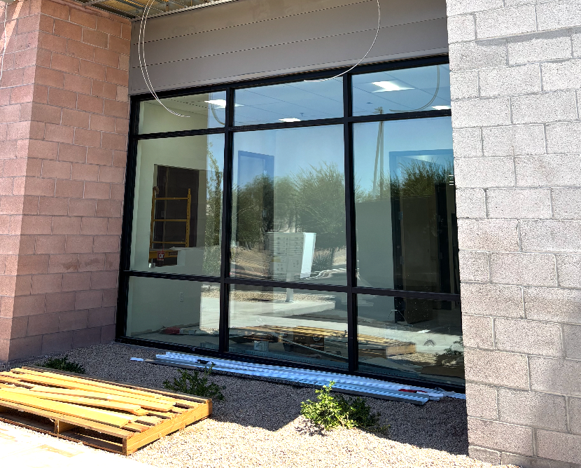 Large window on a building exterior, black frames, reflecting interior construction and landscape.