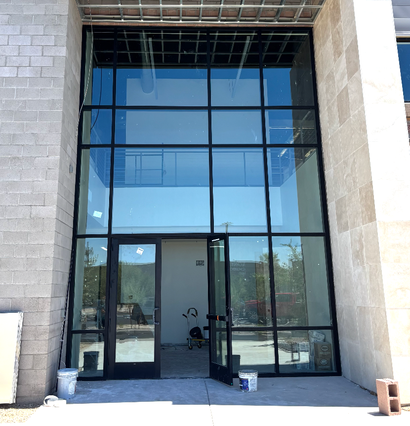Exterior view of a building with a glass facade and open doors, showing the interior, concrete blocks visible.