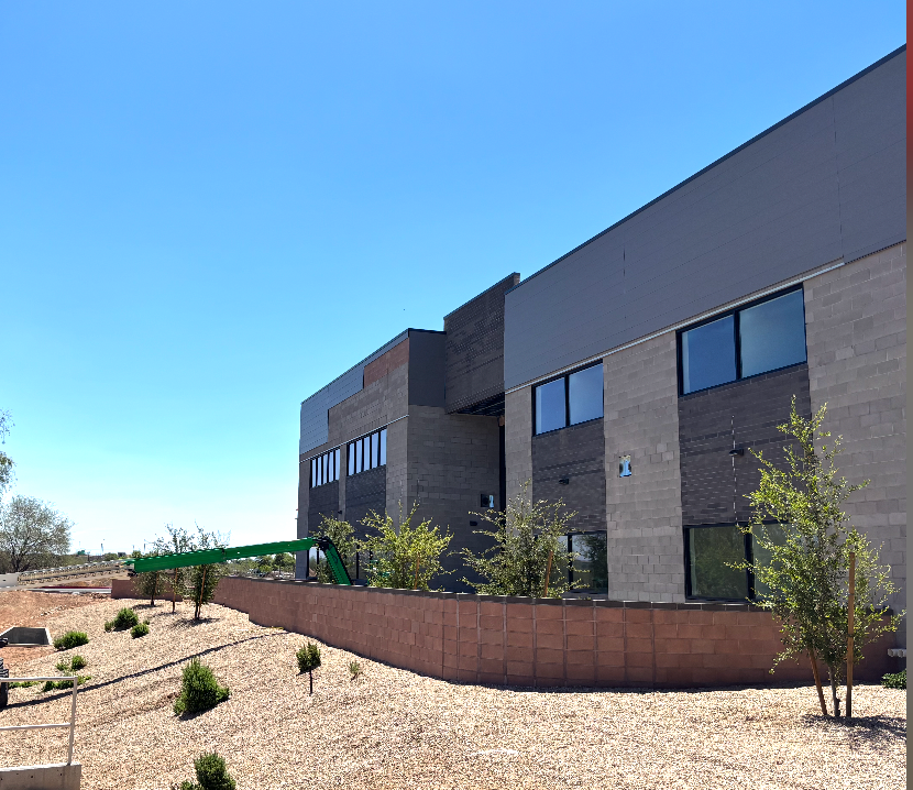 Modern building with grey and tan brick exterior, blue sky, and sparse landscaping.
