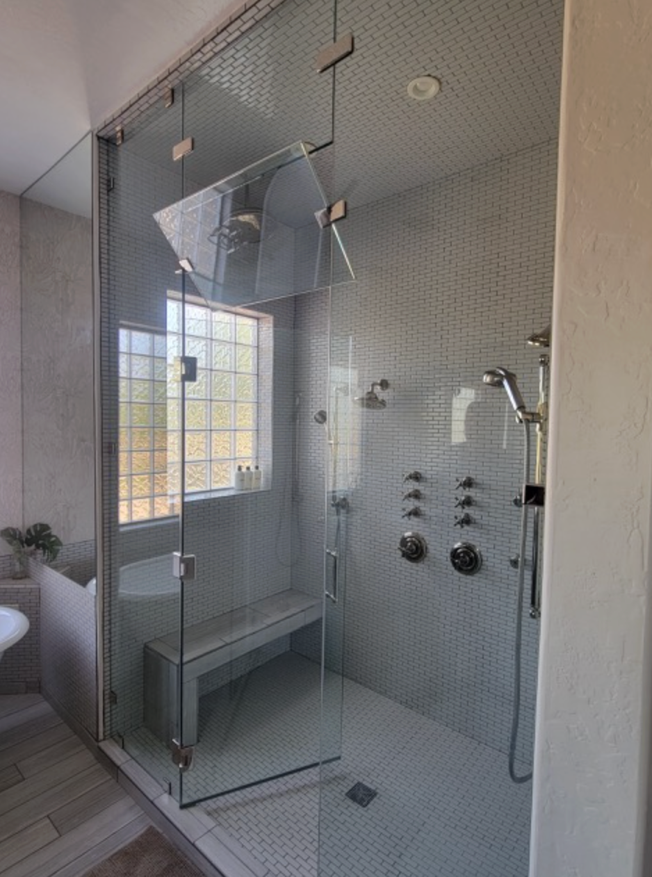 Glass-enclosed shower with bench, multiple shower heads, and mosaic tiled walls.