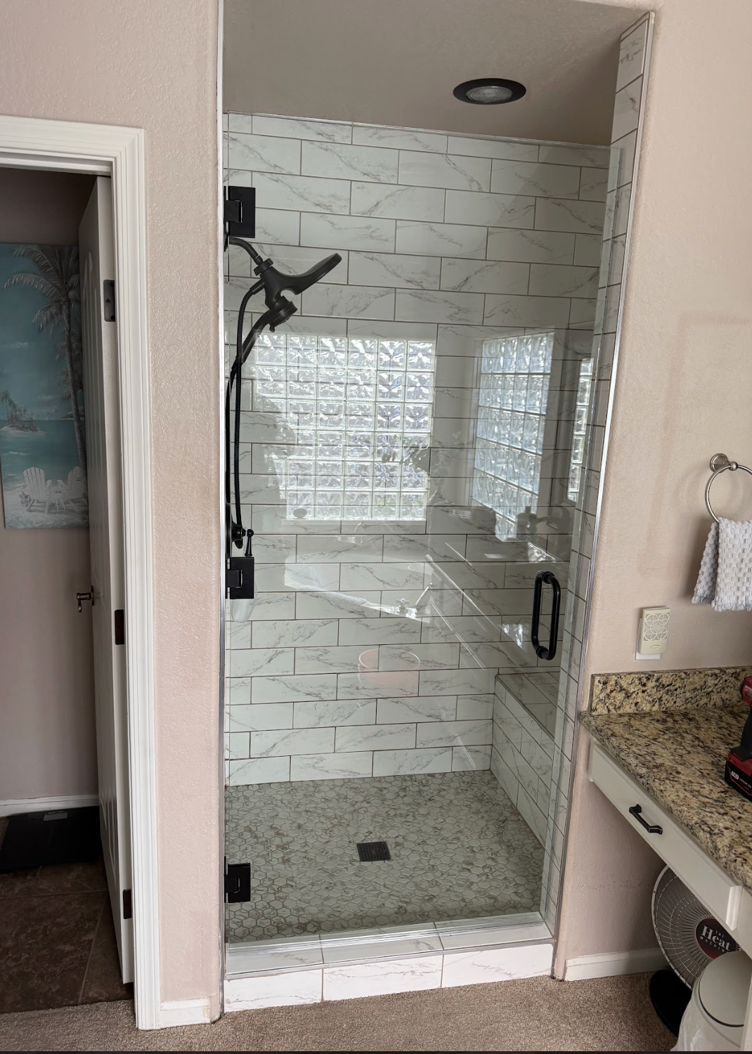 Glass shower with black fixtures and white marble-look tile. Pebble shower floor, glass block window, and built-in bench.