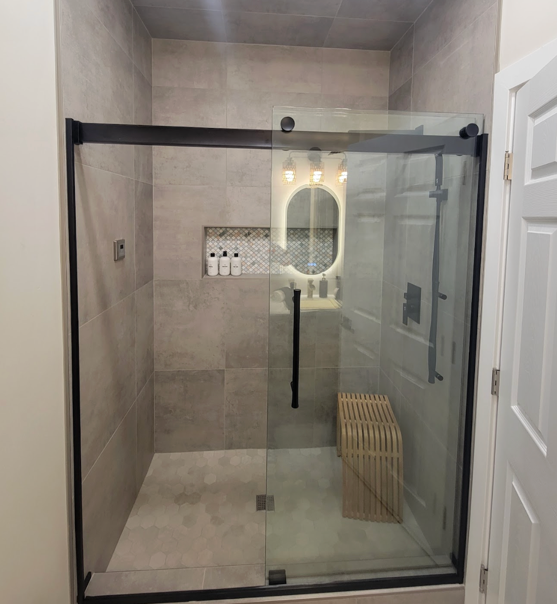 Modern bathroom with glass shower enclosure, beige tiles, and black fixtures.