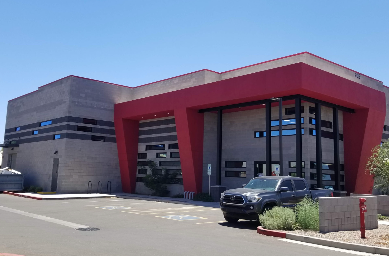Modern building with red entrance canopy and a parked black car on a sunny day