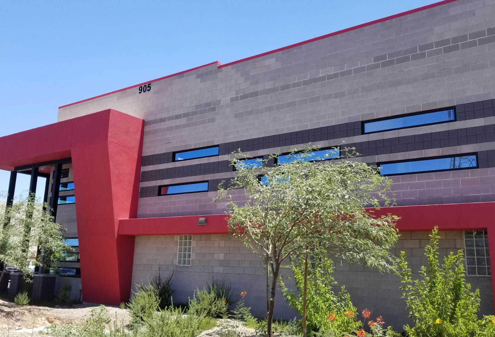 Modern building exterior with red accents, gray walls, and desert landscaping in front