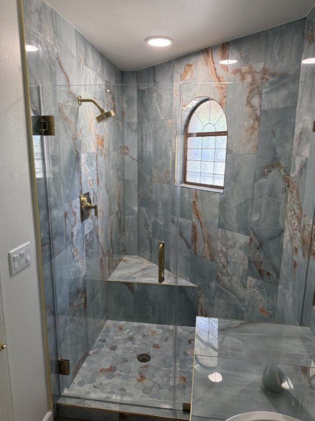 Blue tiled shower with glass doors and gold fixtures; includes a bench and arched window.