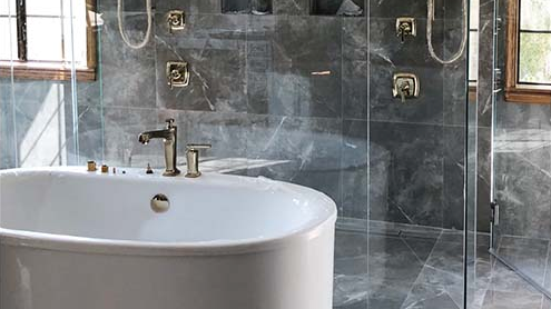 Modern bathroom with a white tub, gray marble walls, and glass shower.