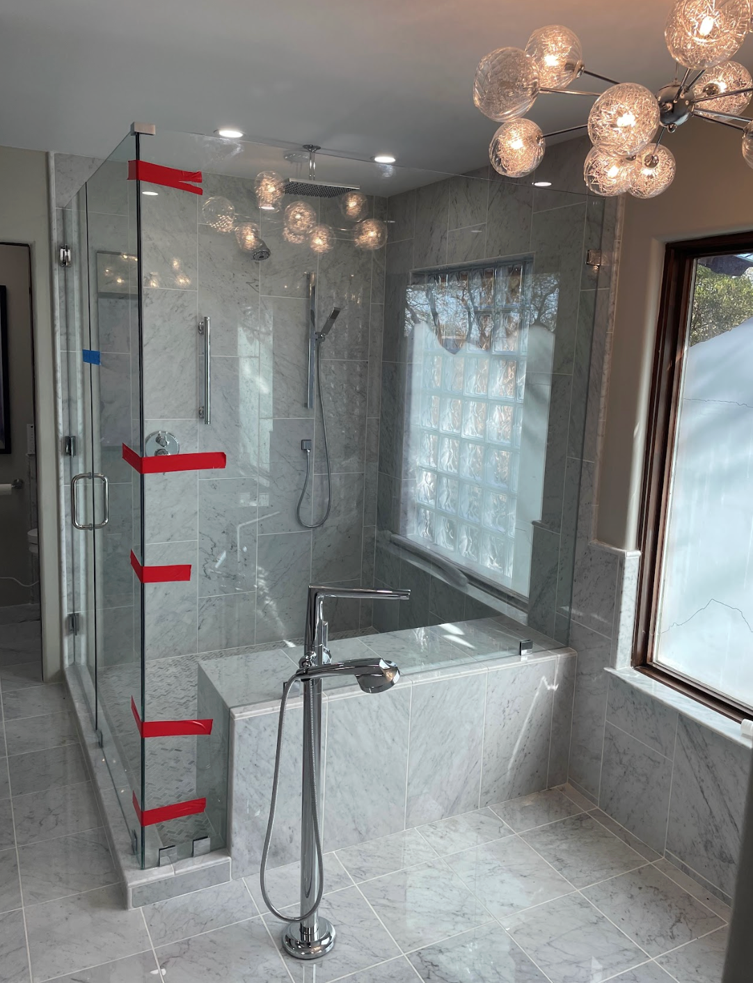 Modern gray bathroom with glass shower, freestanding tub, and large window