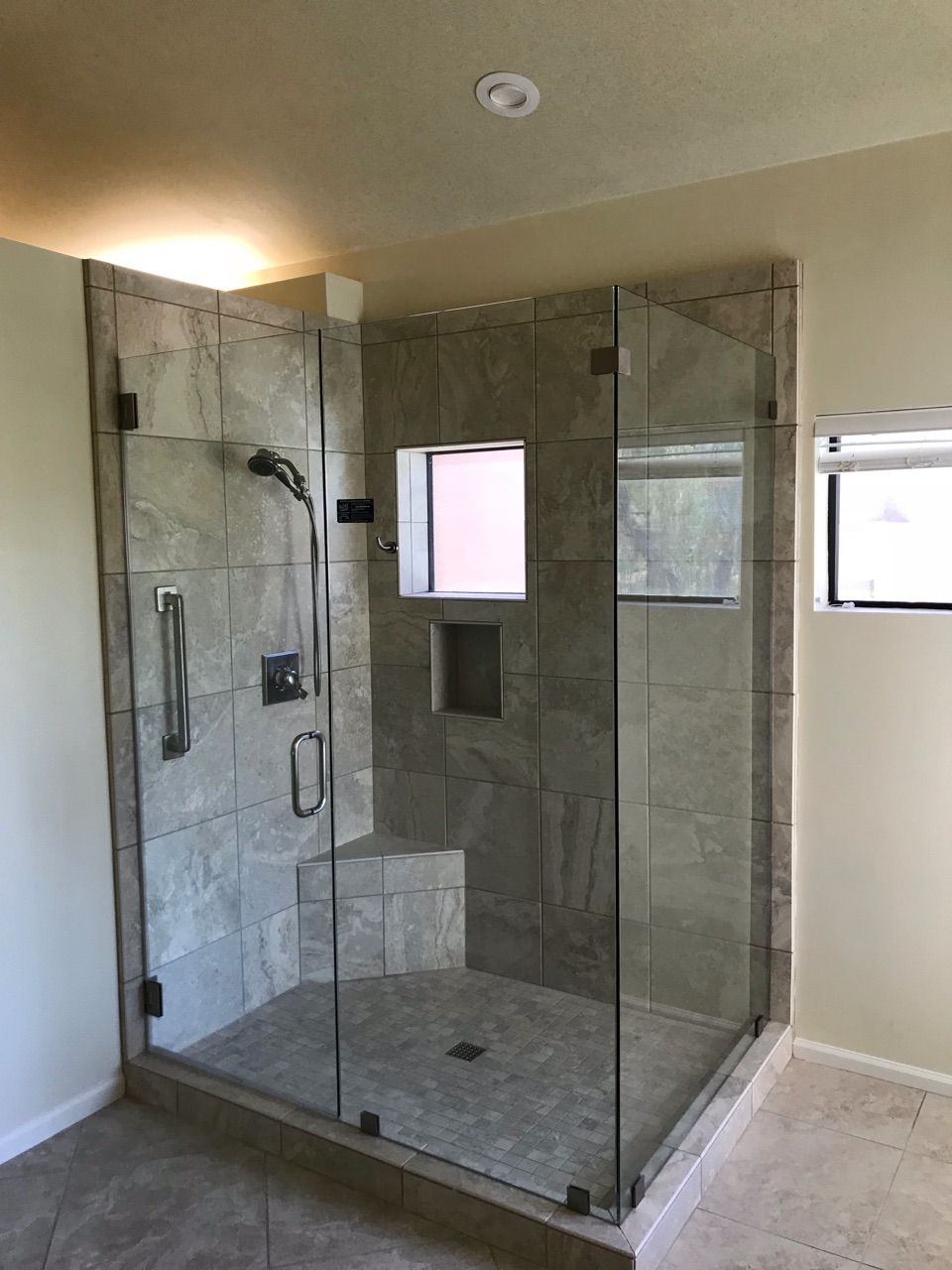 Glass-walled shower with gray tile, a built-in bench, and a small window.