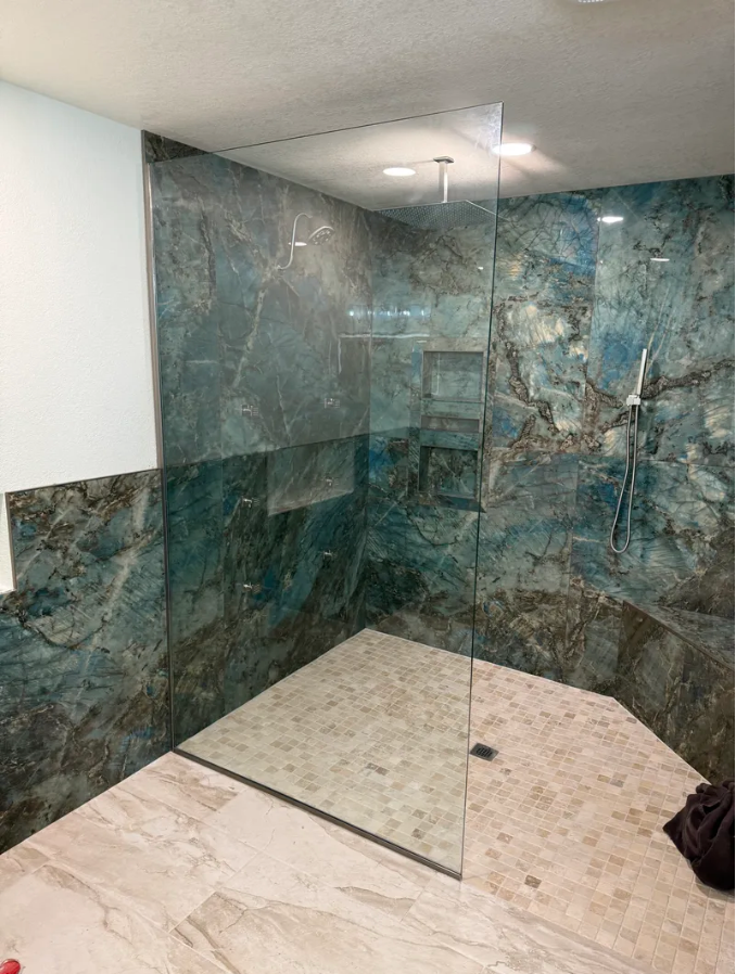 Shower with teal marbled walls, clear glass enclosure, and light stone tile floor.