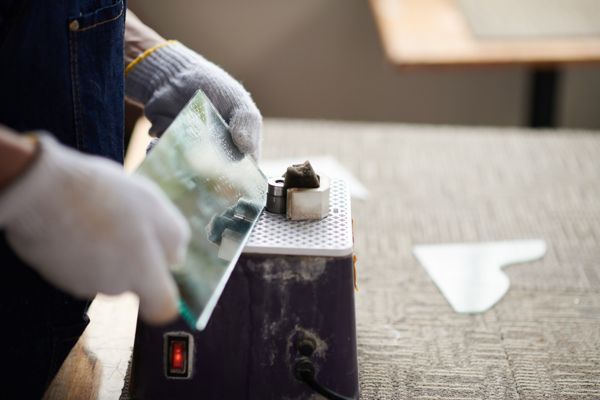 Person wearing gloves cutting glass with a cutting tool on a workbench.