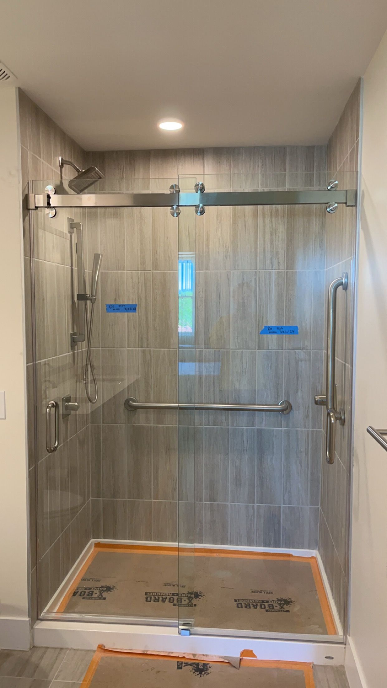 Accessible shower stall with grab bars, glass door, and tiled walls.