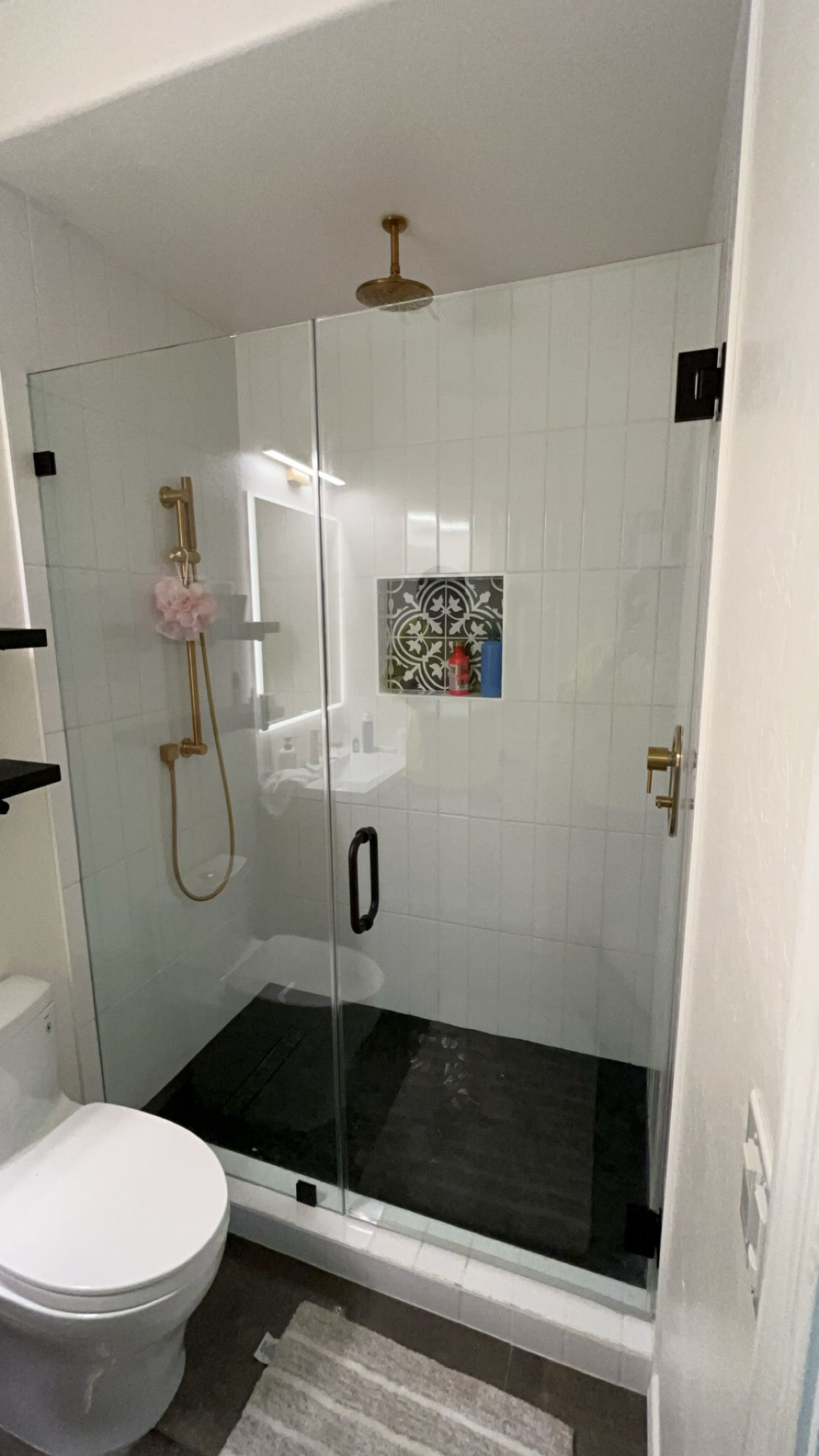 Modern bathroom with glass shower, black floor, white tiled walls, gold fixtures, and a toilet.