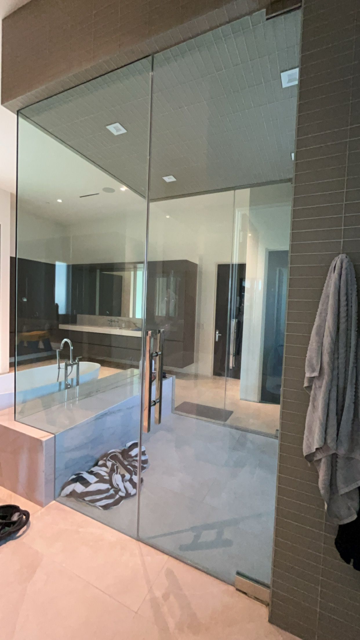A large glass shower with a towel on the right and a bathroom in the background.