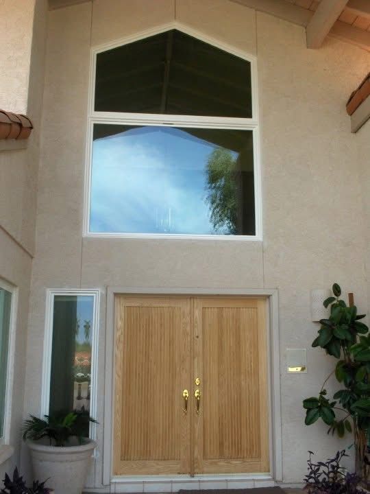 Front entrance with double wooden doors, tall windows, and potted plants under a peaked archway.