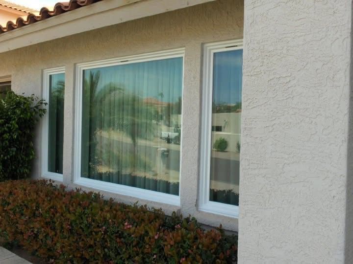 House exterior with a large window, white stucco wall, and shrubs in front