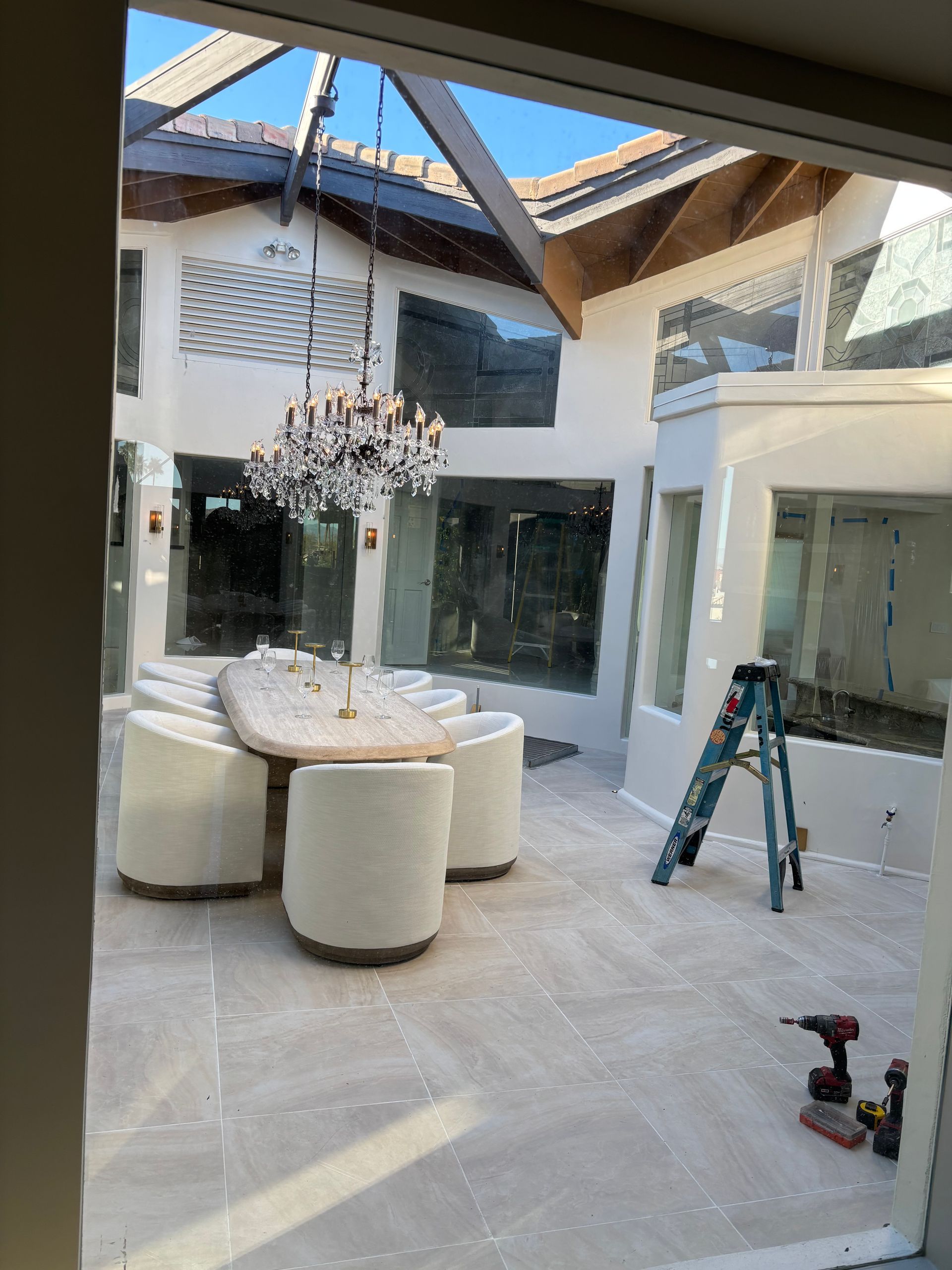 Courtyard with dining table, chandelier, and white walls. Ladder leans against wall.