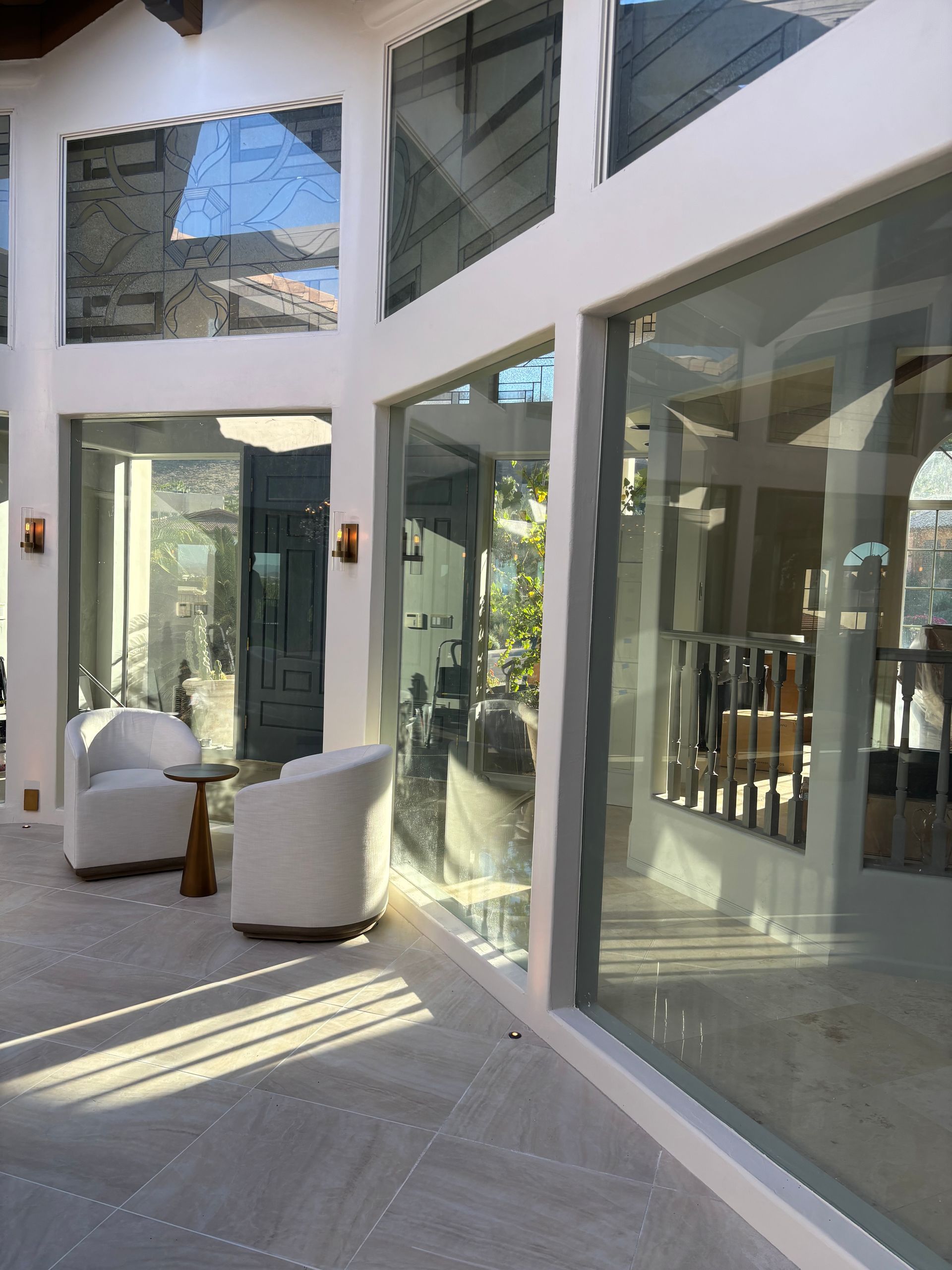 Sunlit interior with large windows, white walls, two chairs, and a small table.