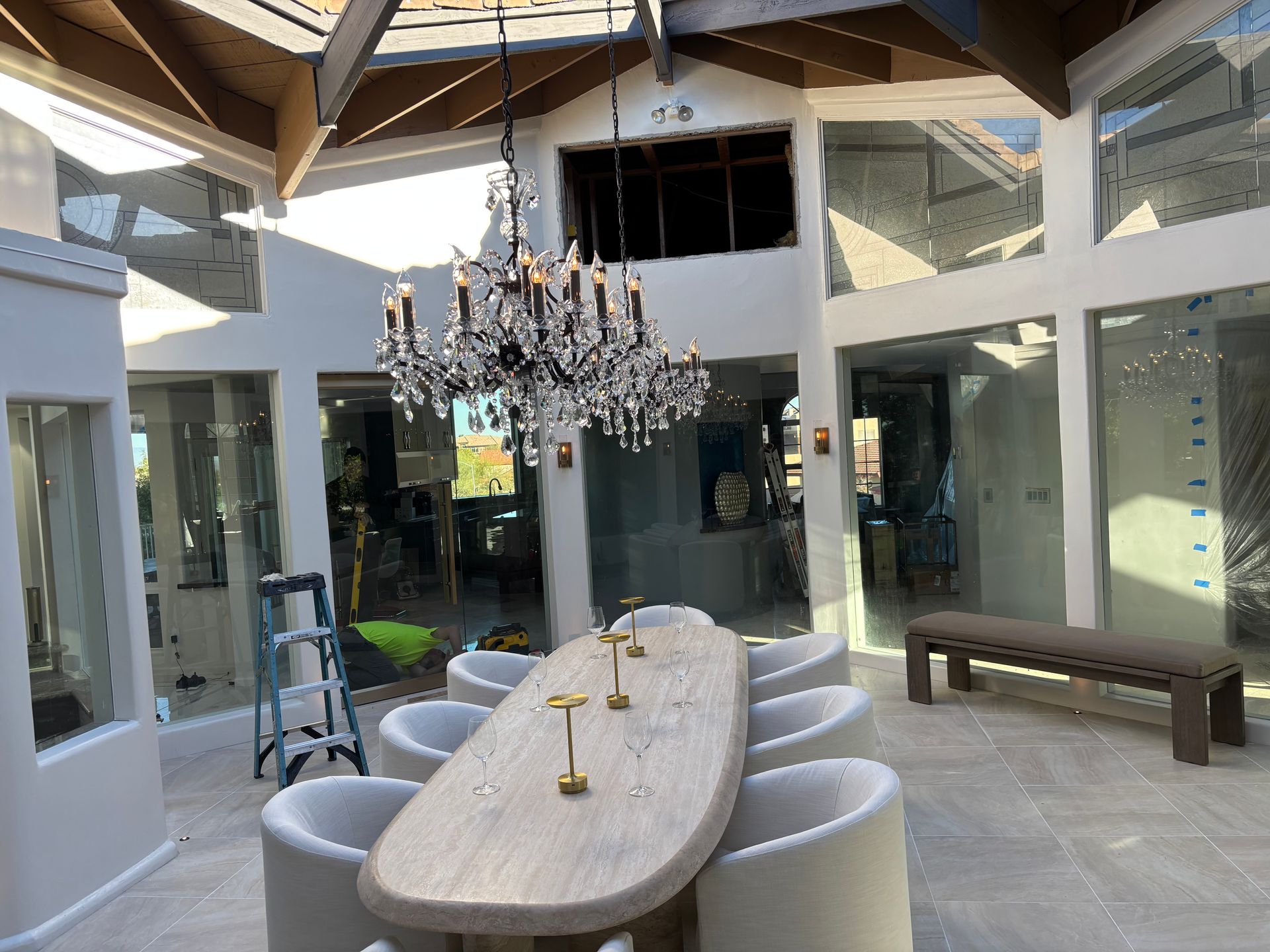 Elegant patio dining area with chandelier, long oval table, and white chairs under a wood-beamed roof