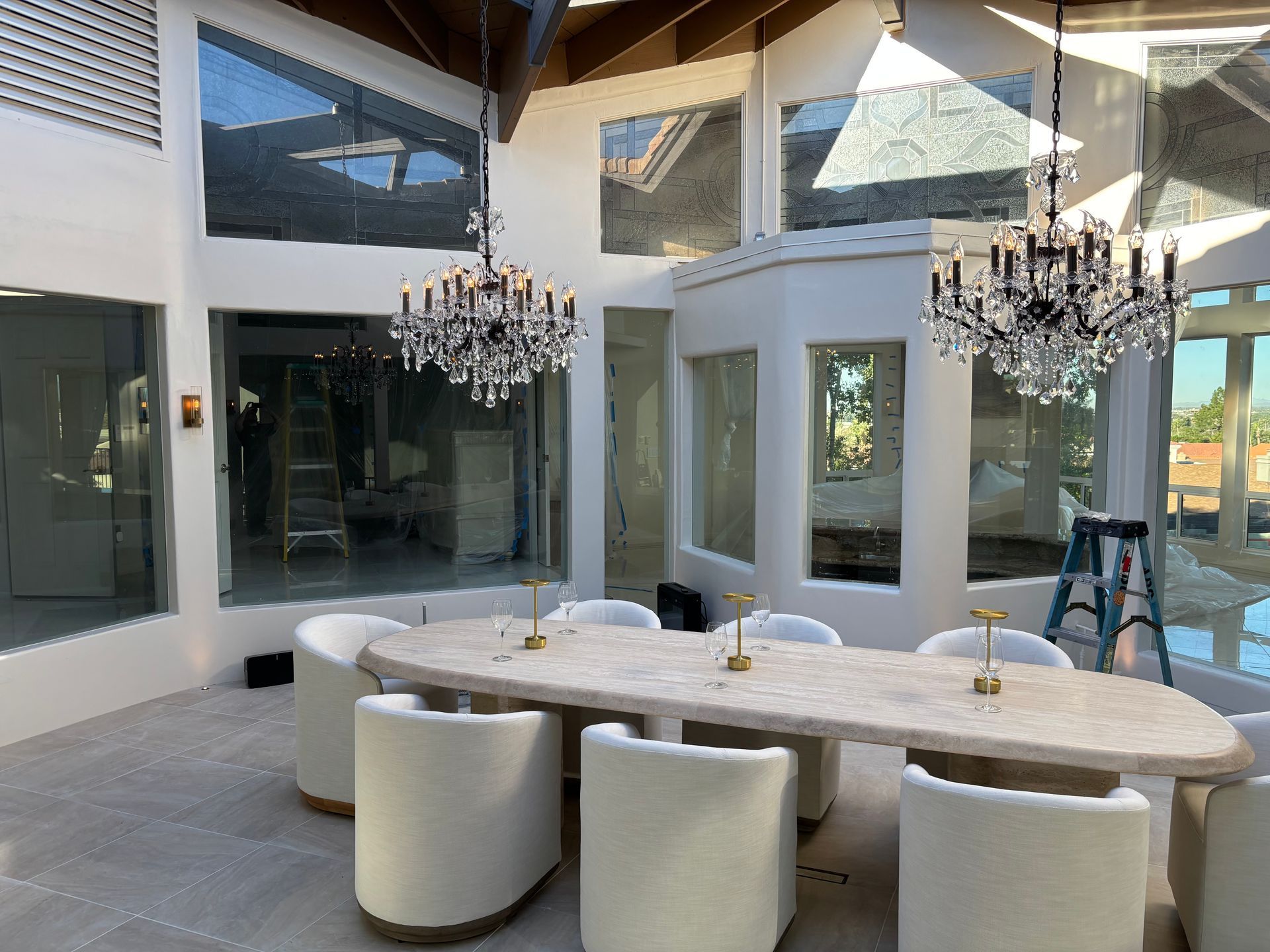 Elegant dining room with large windows, chandeliers, and oval table set for guests.
