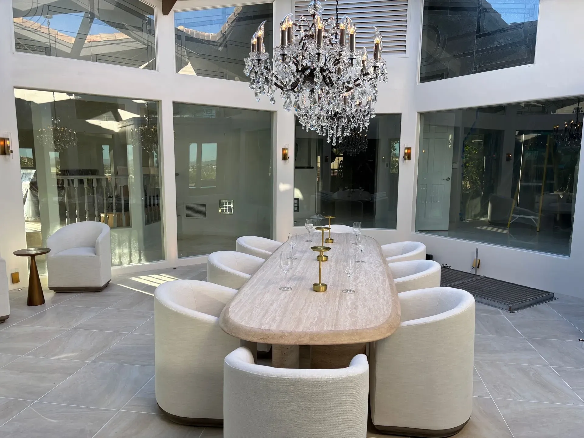 Modern dining room with white chairs, long table, chandelier, and glass walls in a bright atrium