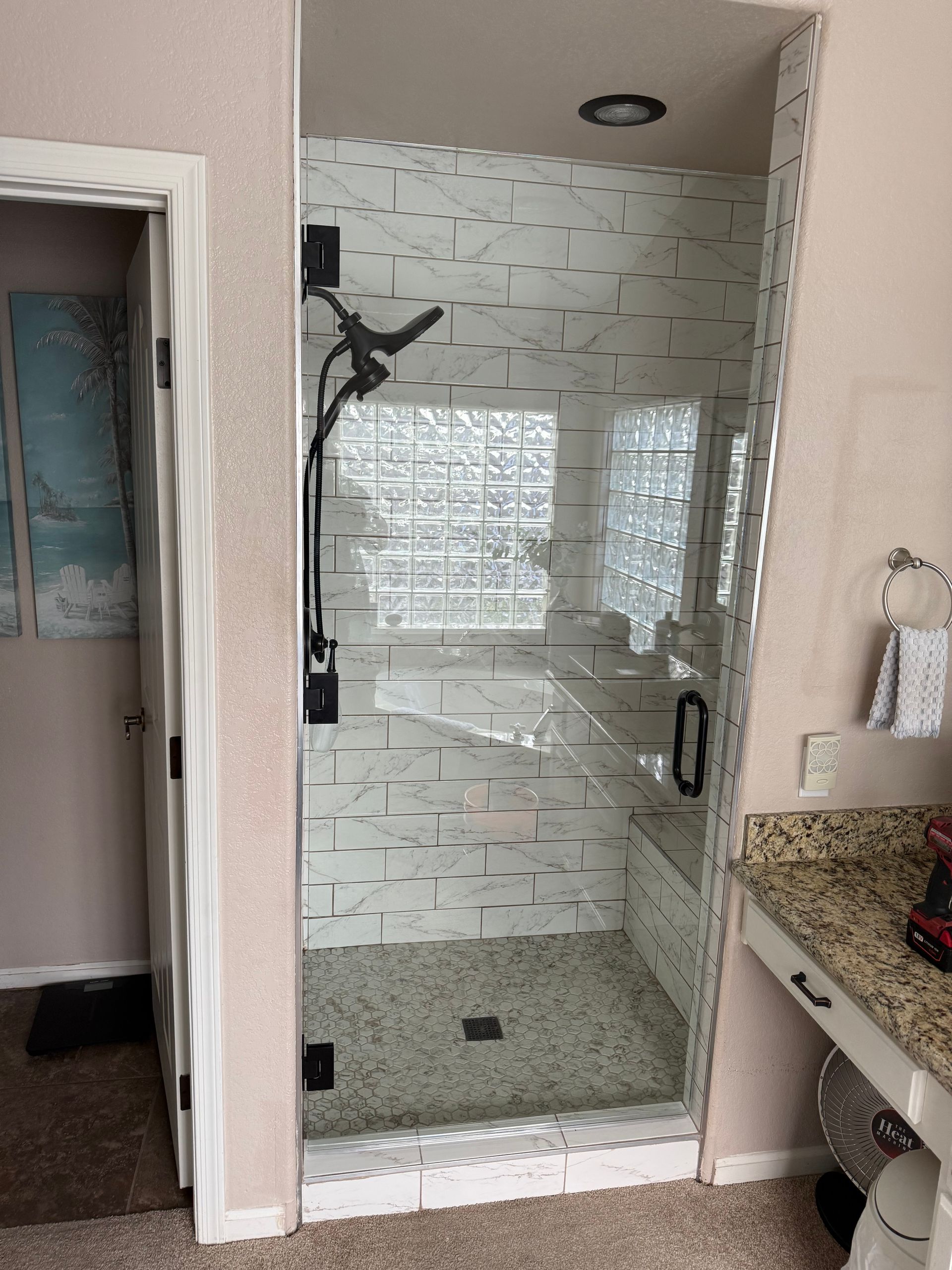 A walk-in shower with clear glass walls, marble tile, and a pebble floor; adjacent to a bathroom vanity.