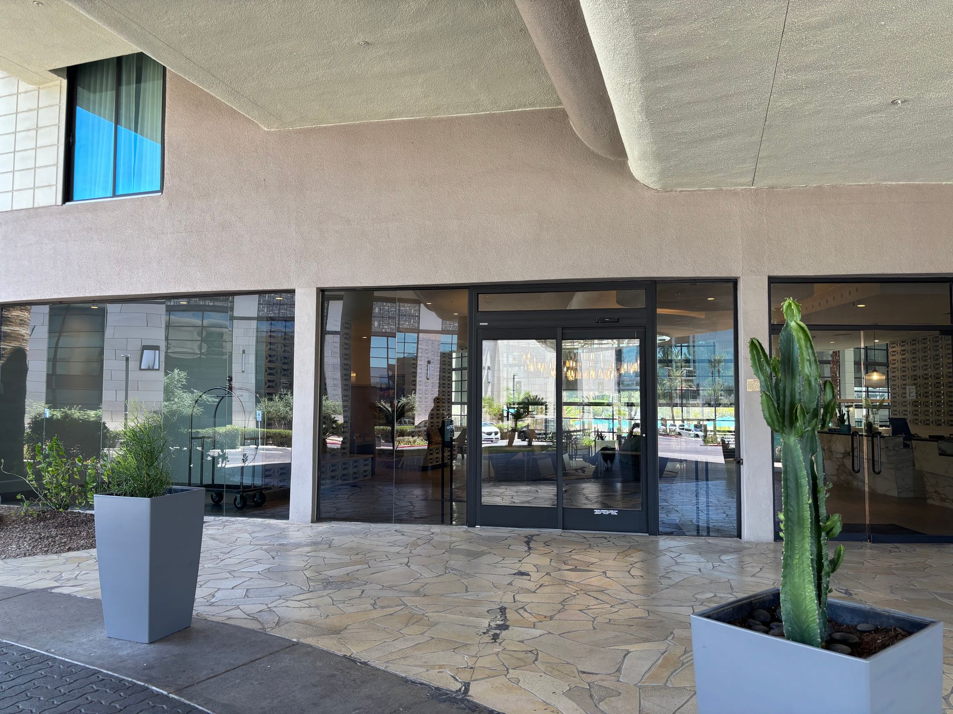 Exterior of a building with a glass entrance, featuring a cactus in a gray planter.