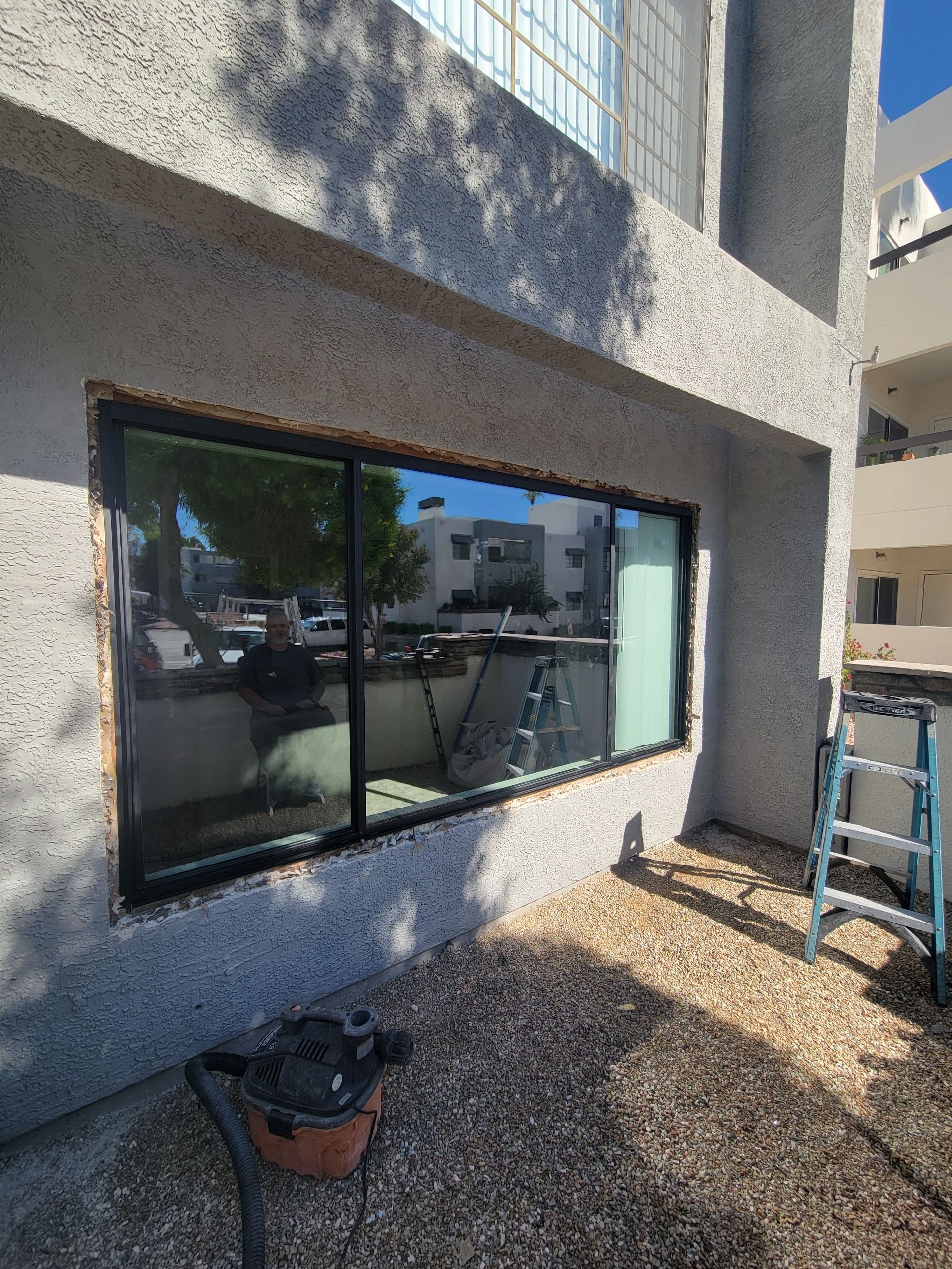 A new window installed in an exterior wall with stucco. A ladder and vacuum are visible nearby.