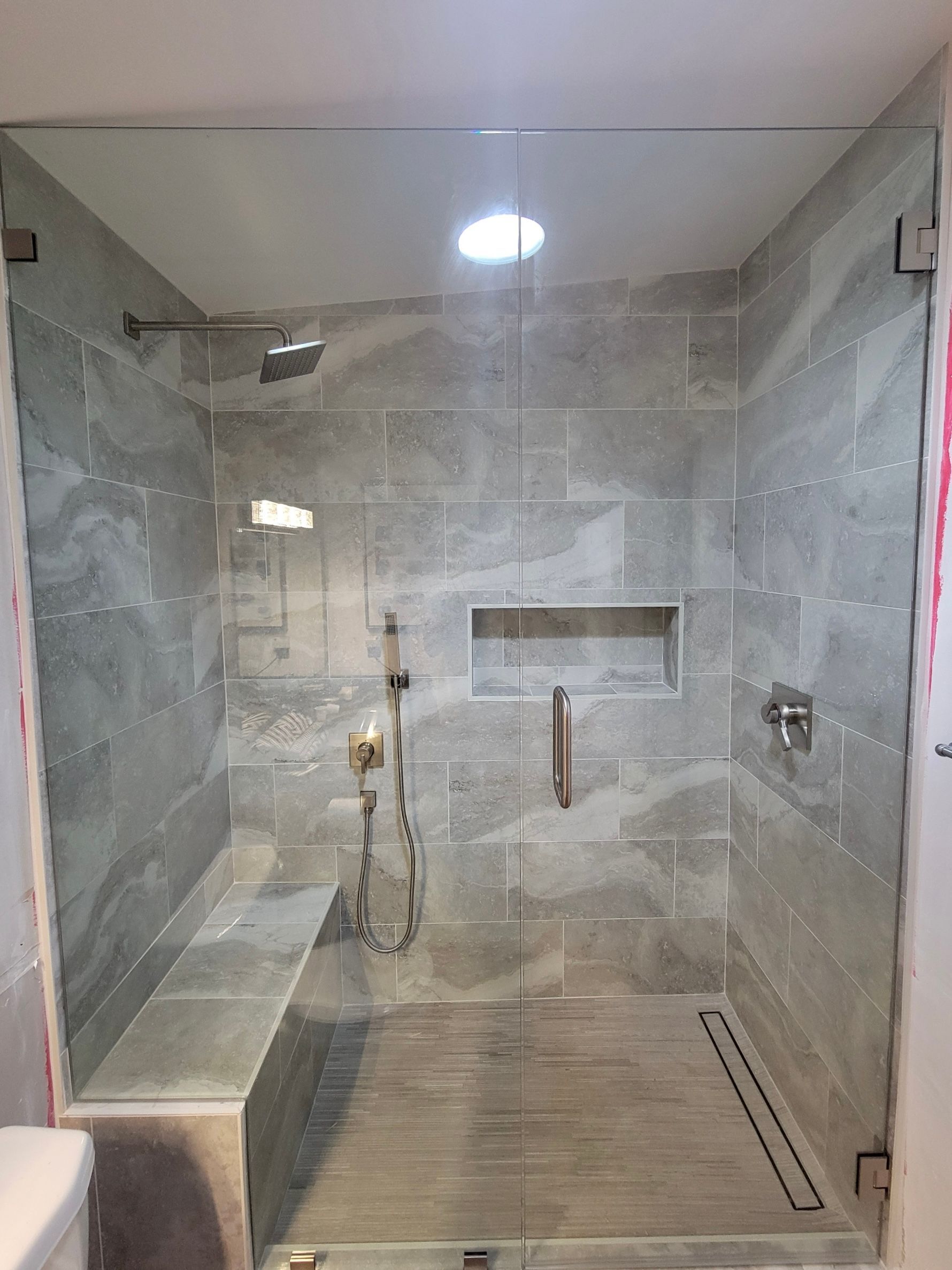 Modern shower with gray tiled walls, glass door, and built-in bench.