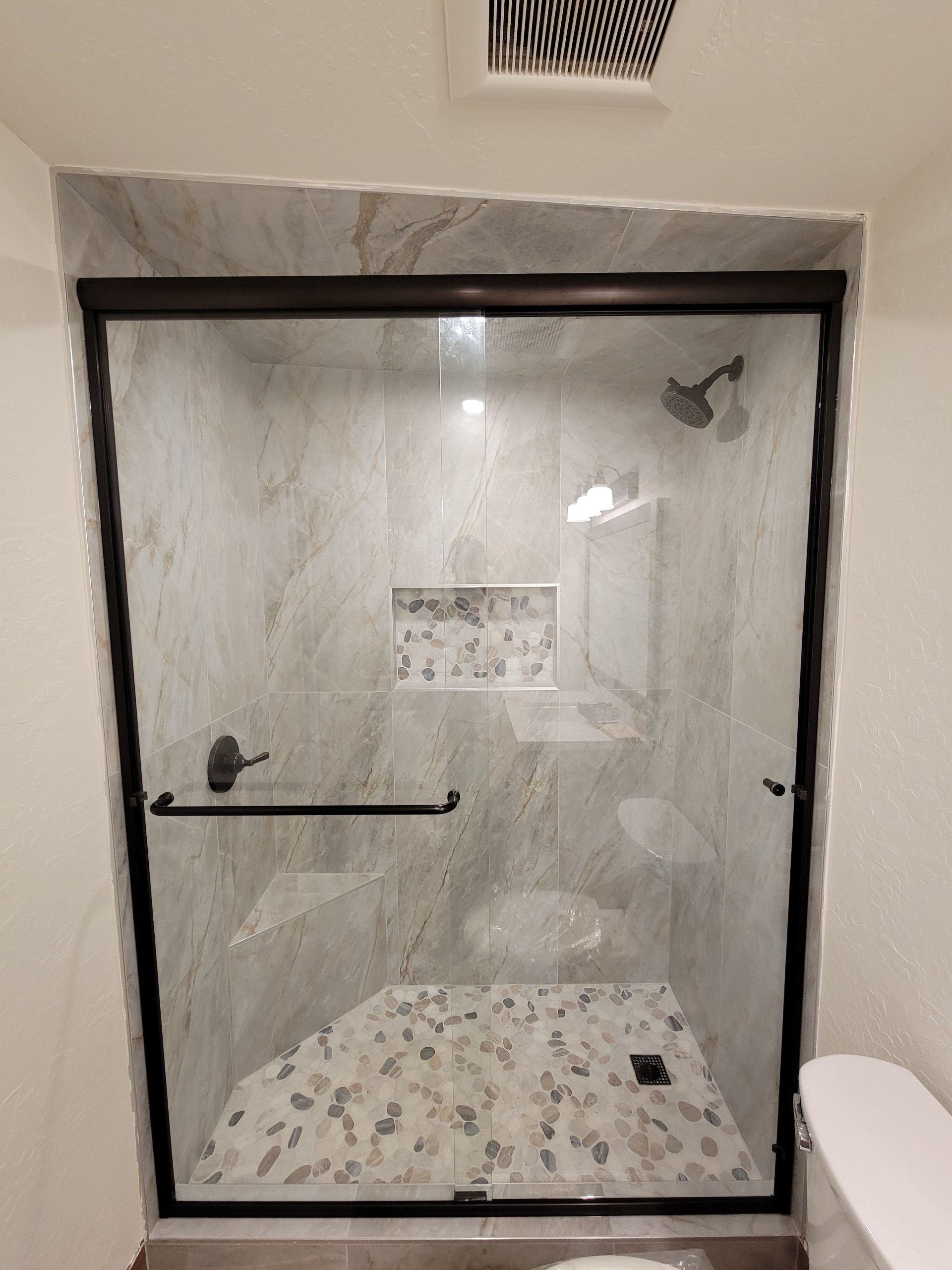 Shower with glass door and black frame, light marble tiles, and stone floor.