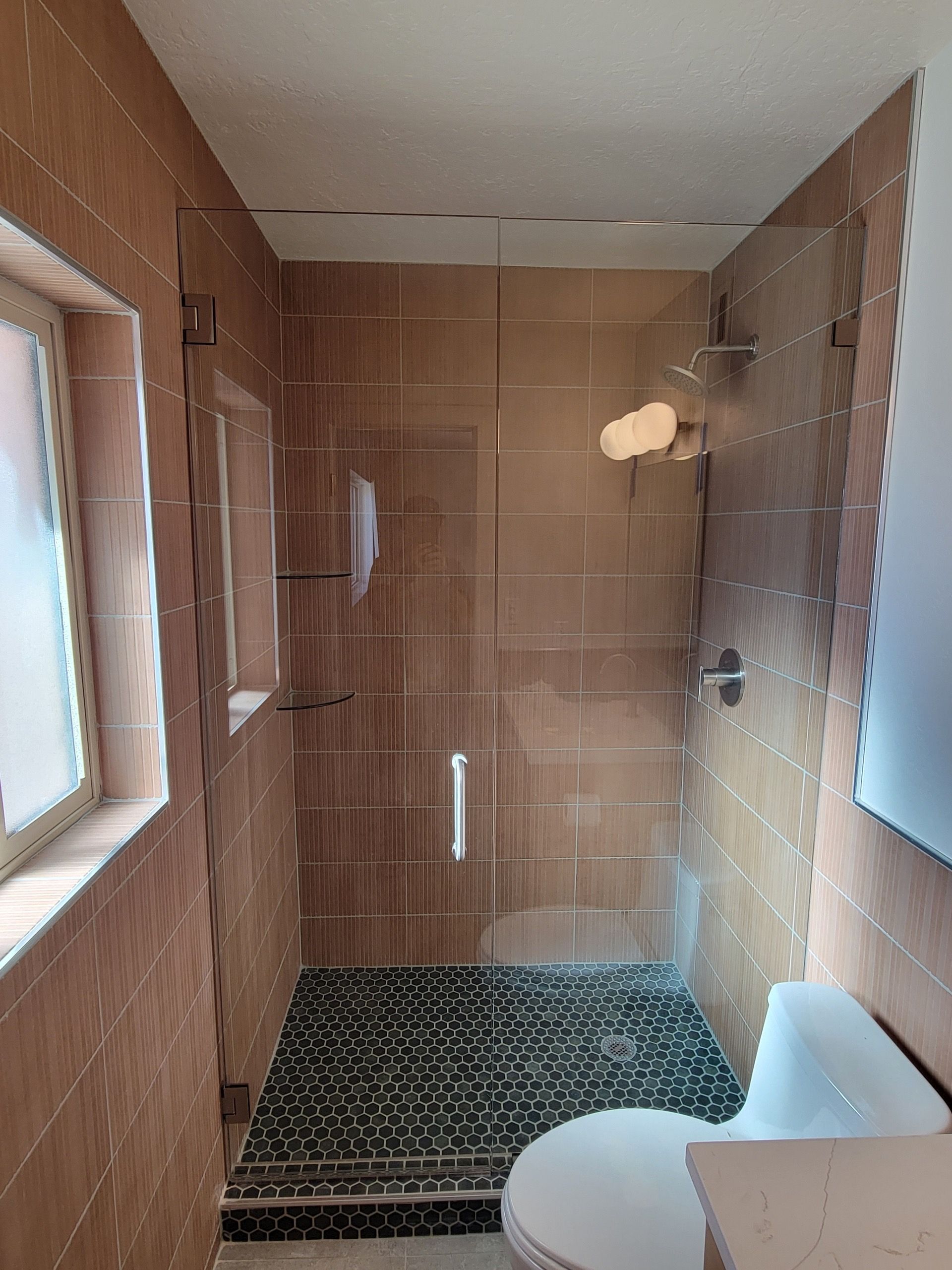 Bathroom with glass shower doors, brown tiled walls, and pebble floor. A toilet is visible.