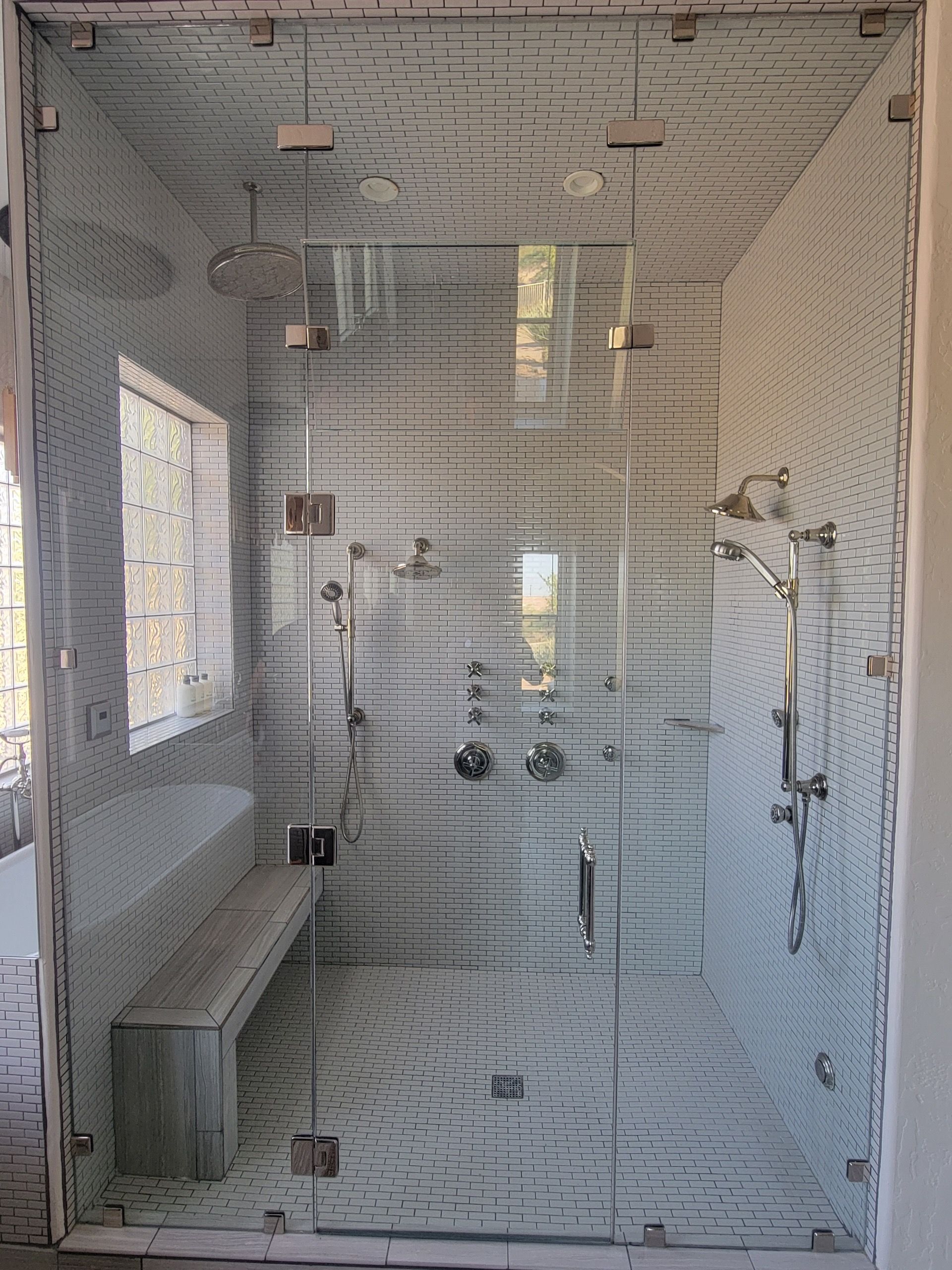 Glass-enclosed shower with wooden-look tiled walls, bench, and multiple showerheads.