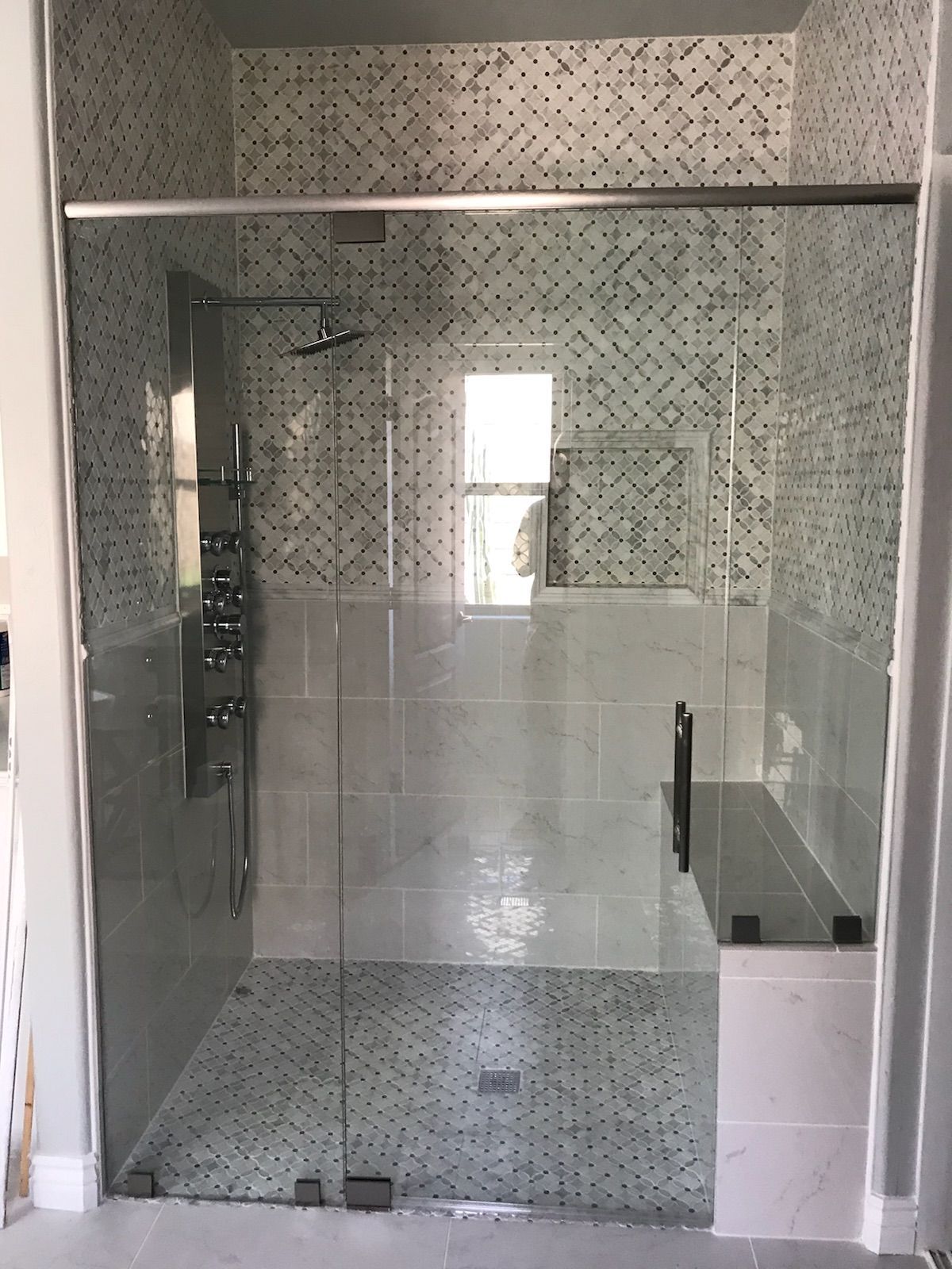 Glass-enclosed shower with mosaic tile walls and floor; chrome fixtures.