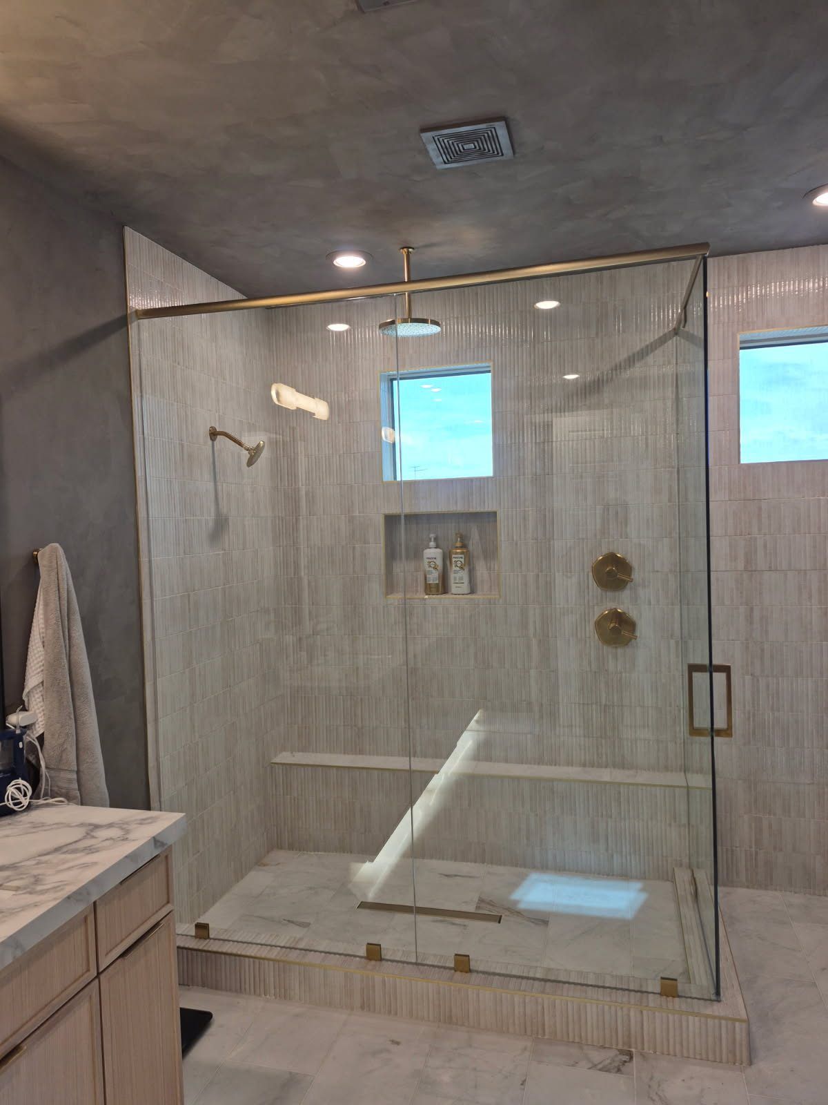 Ceiling-height frameless glass shower with brushed gold hardware and bench in a Scottsdale area bathroom by ABC Glass
