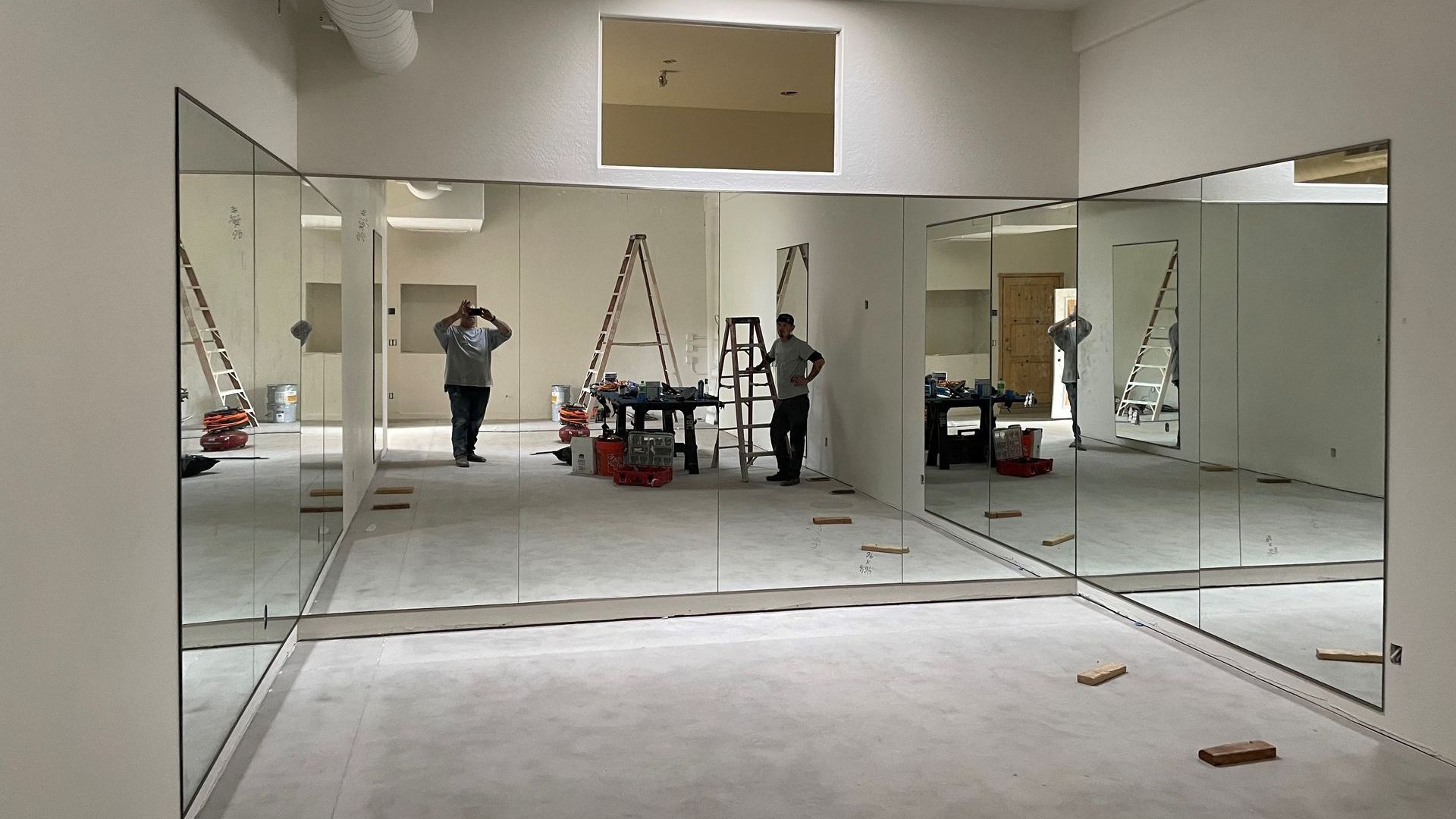 Installation of large mirrors in a dance studio. Workers are visible, with ladders and equipment on the floor.