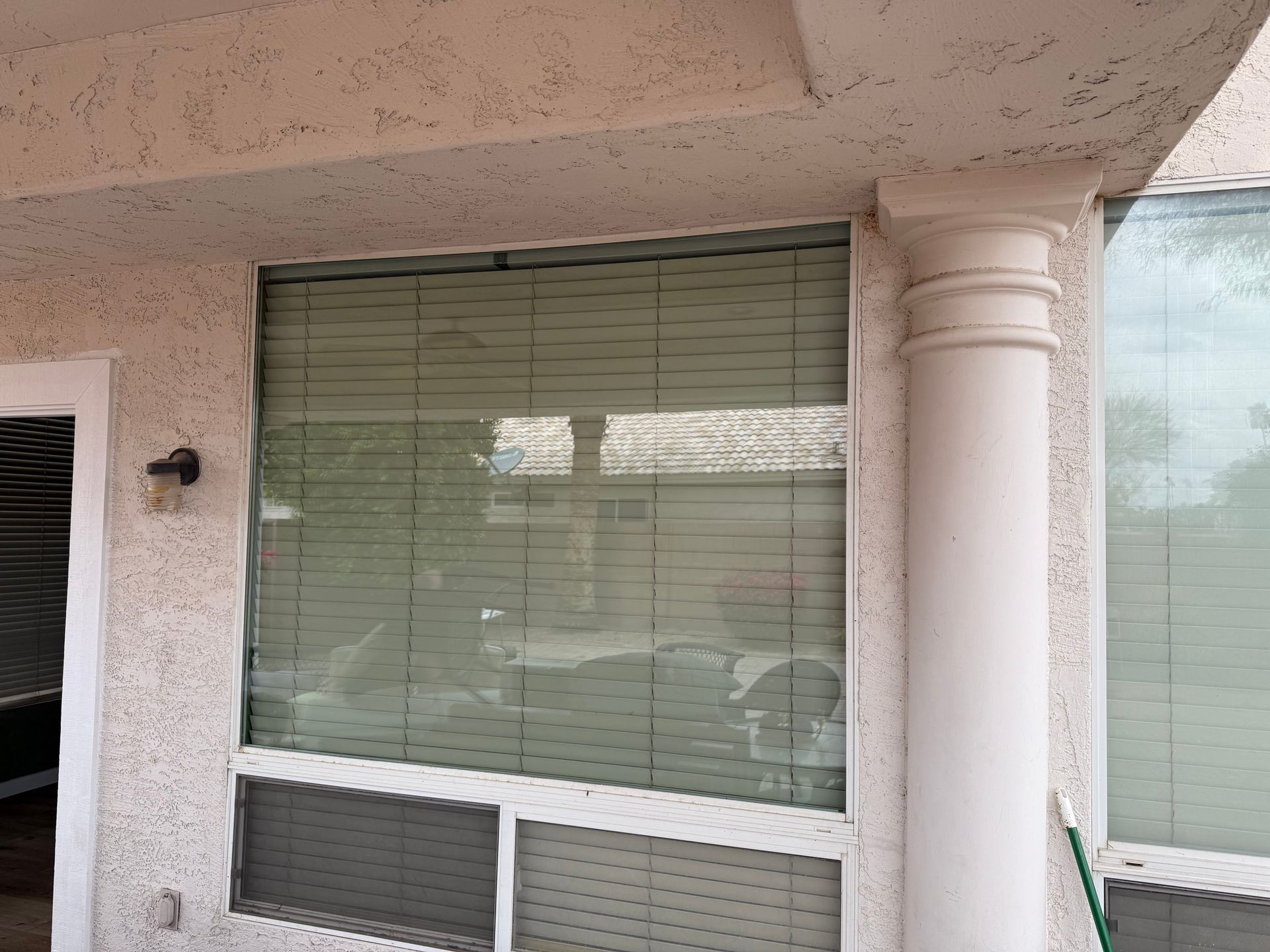 Window with closed blinds, next to a white column, on an exterior stucco wall.