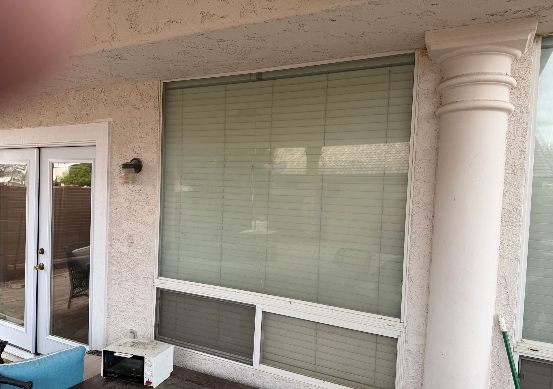 Exterior view of building with large window covered in blinds, next to a white column.