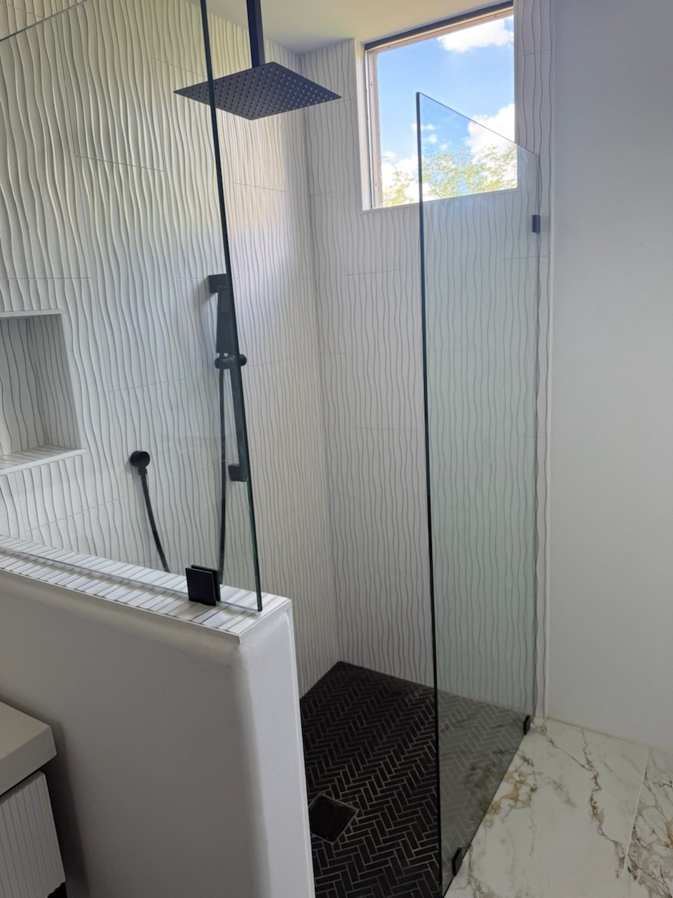 Modern bathroom shower with textured white tile walls, black fixtures, and a glass door.