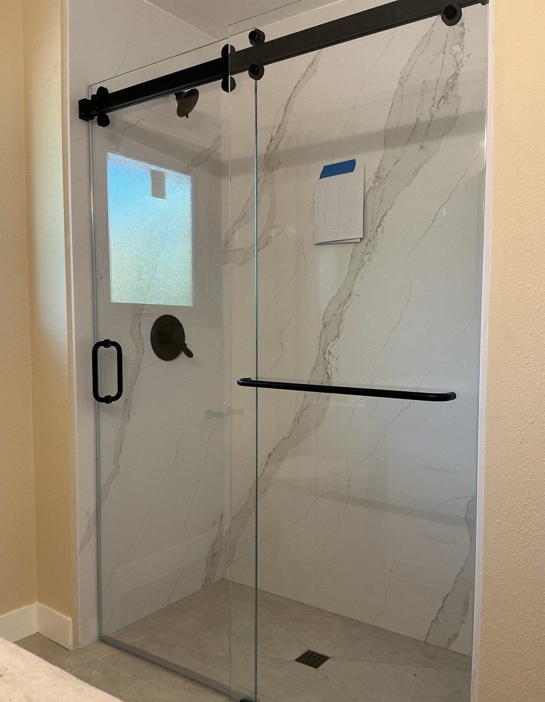 Frameless barn style sliding shower door with matte black roller bar and towel bar installed by ABC Glass in Phoenix
